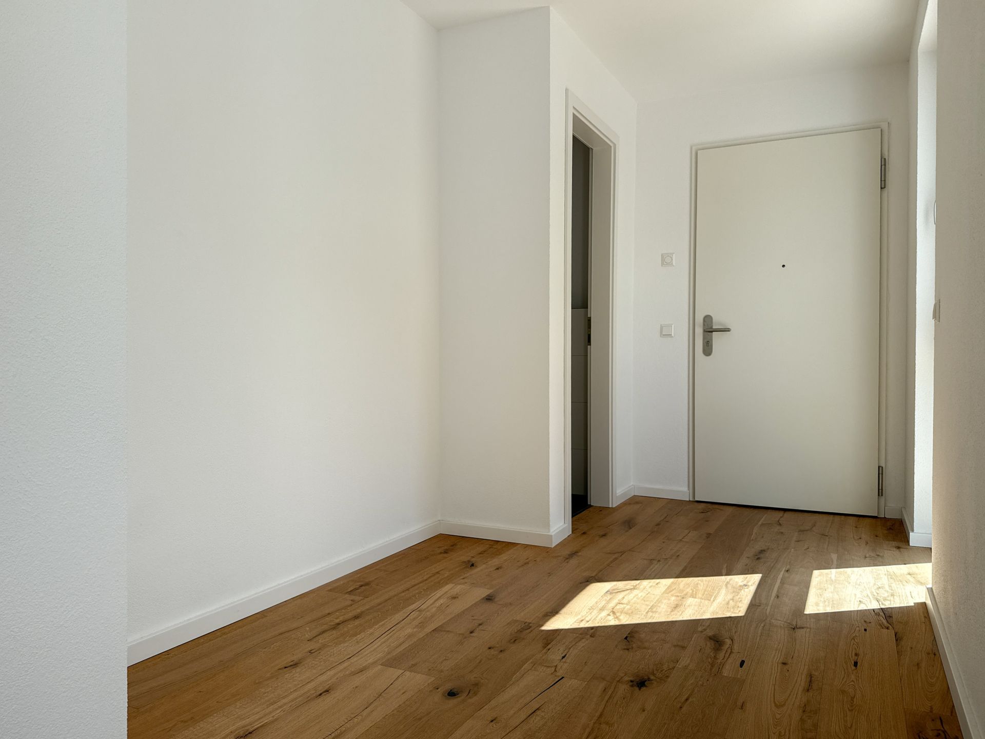 Heller Flur mit Holzboden, weißer Wand und einer geschlossenen weißen Tür.