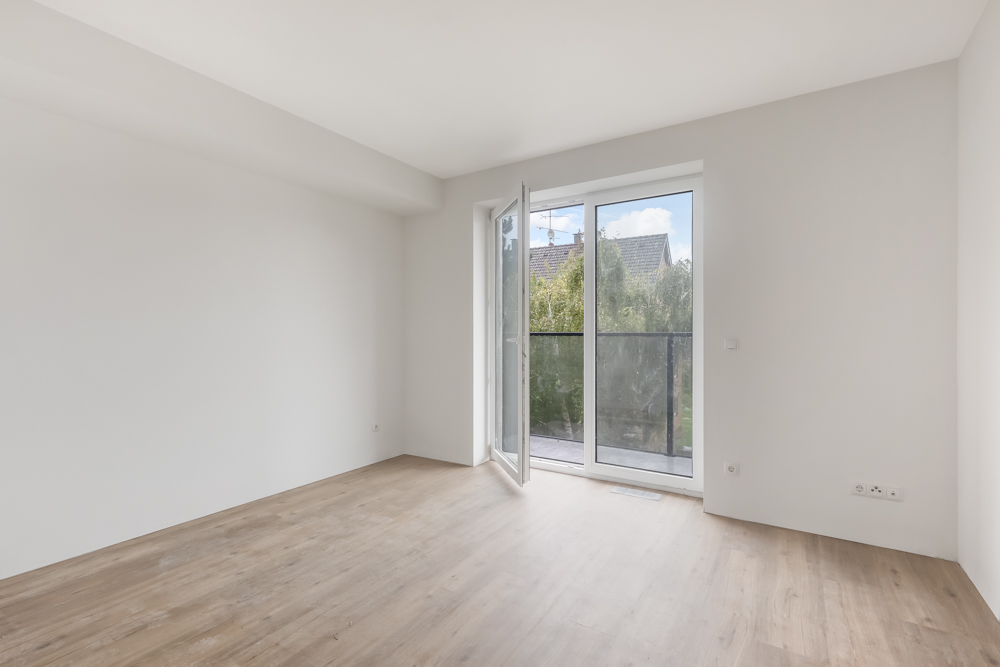 Heller leerer Raum mit Holzboden und großer Glastür zu einem Balkon.