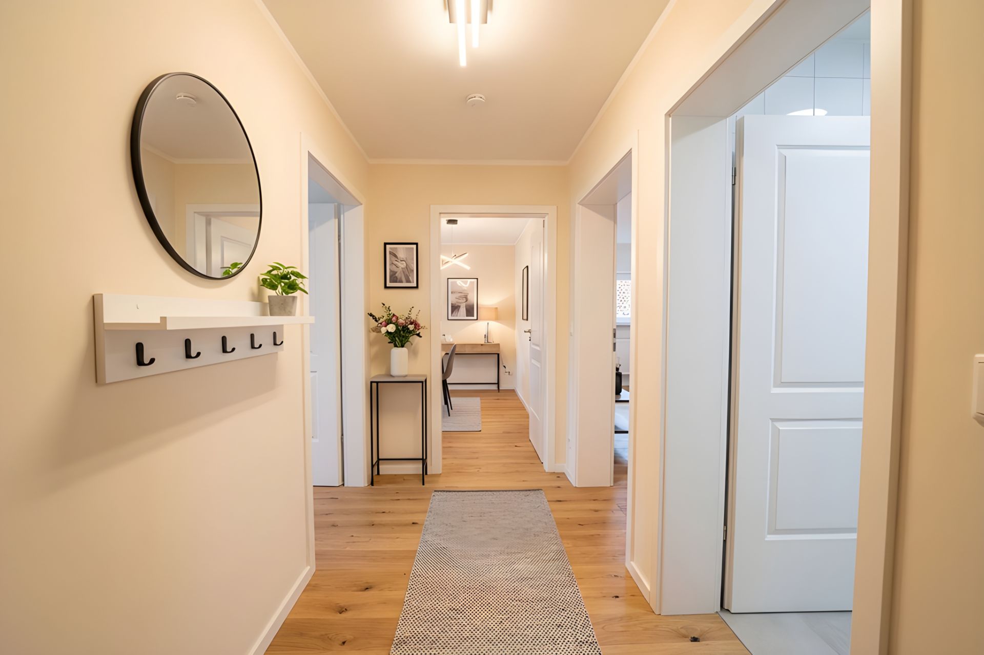 Heller Flur mit Holzboden, rundem Spiegel, Garderobe und mehreren offenen Türen.