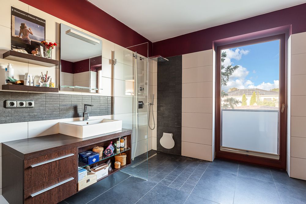 Modernes Badezimmer mit großem Fenster, Waschbecken, Duschkabine und dunklem Boden.