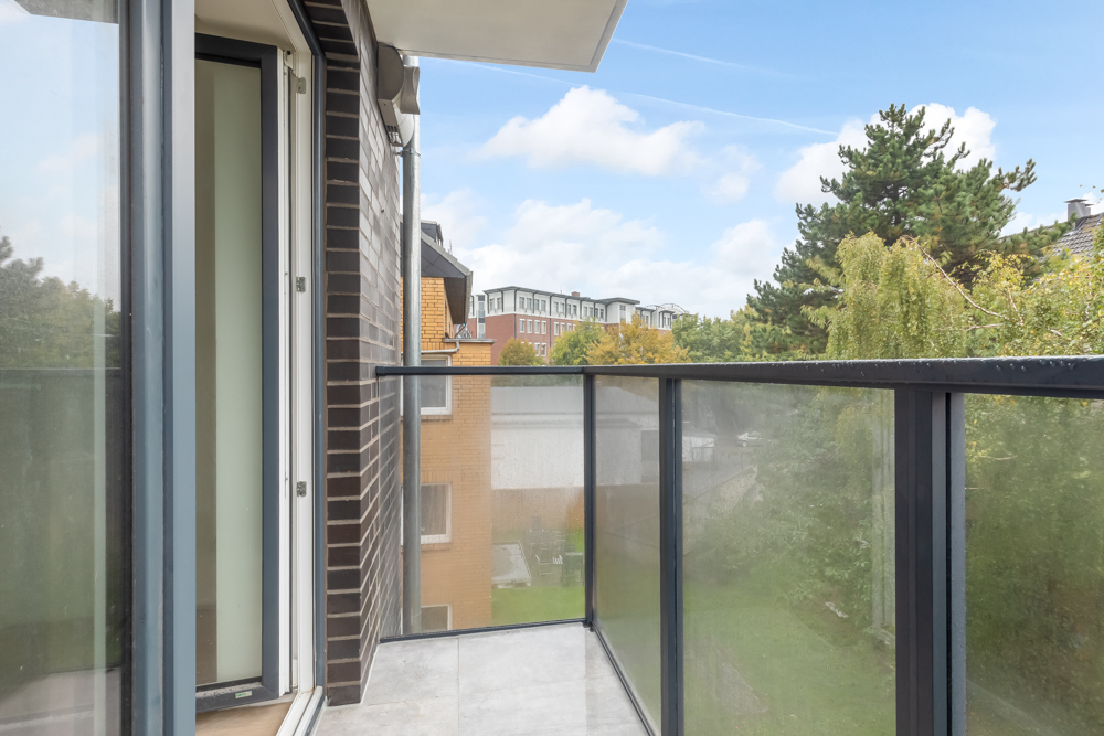 Moderner Balkon mit Glasgeländer und Blick auf Bäume und Nachbargebäude.