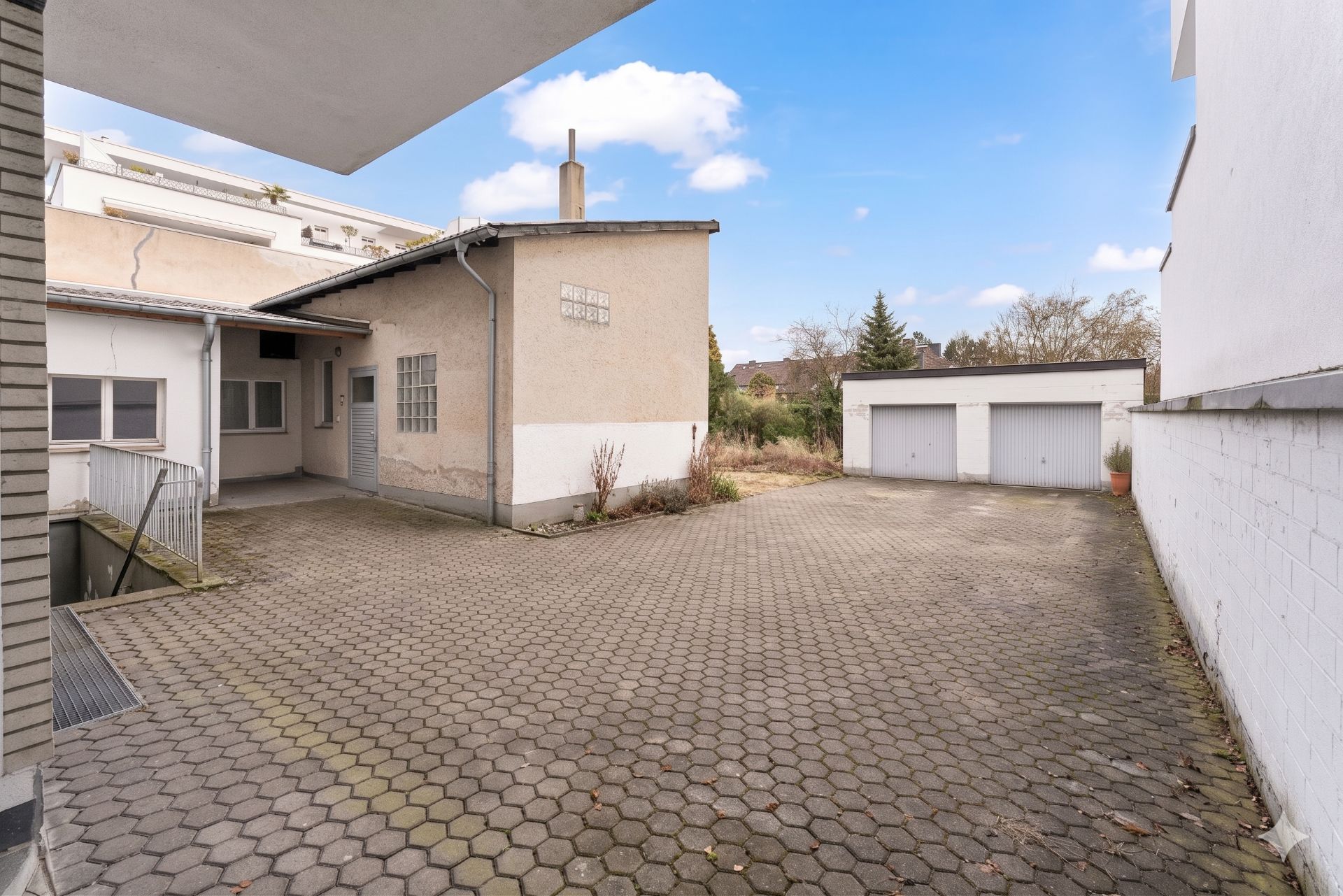 Gepflasterter Innenhof mit Garage, Nebengebäude und etwas Vegetation im Hintergrund.