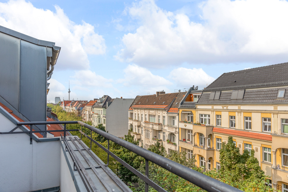 Blick von einem Balkon auf eine Wohnstraße mit Altbauten und Bäumen.