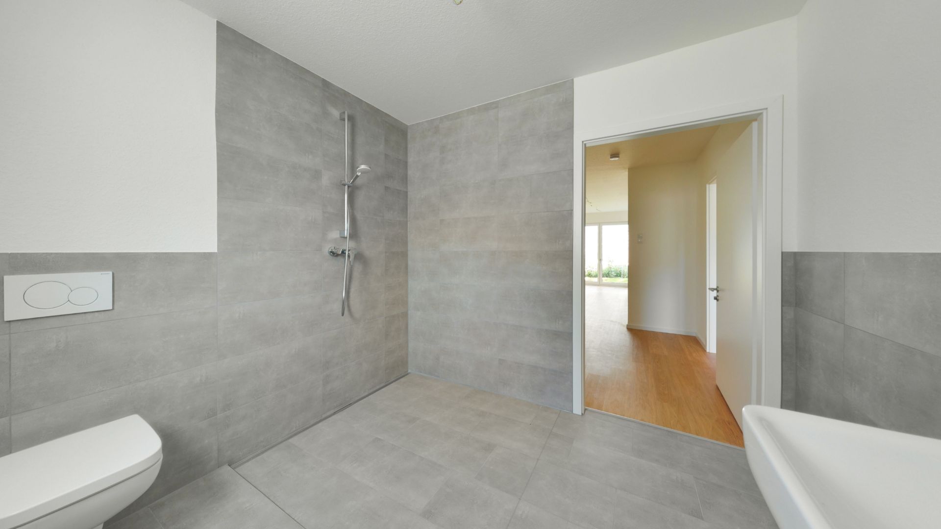 Modernes Badezimmer mit grauen Fliesen, Toilette, Dusche und Waschbecken.