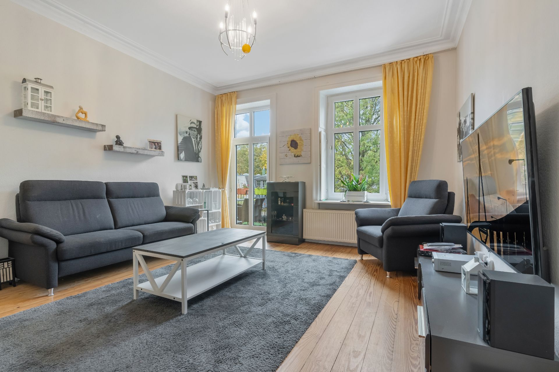 Modernes Wohnzimmer mit grauem Sofa, Sessel, Couchtisch und gelben Vorhängen vor Fenstern.