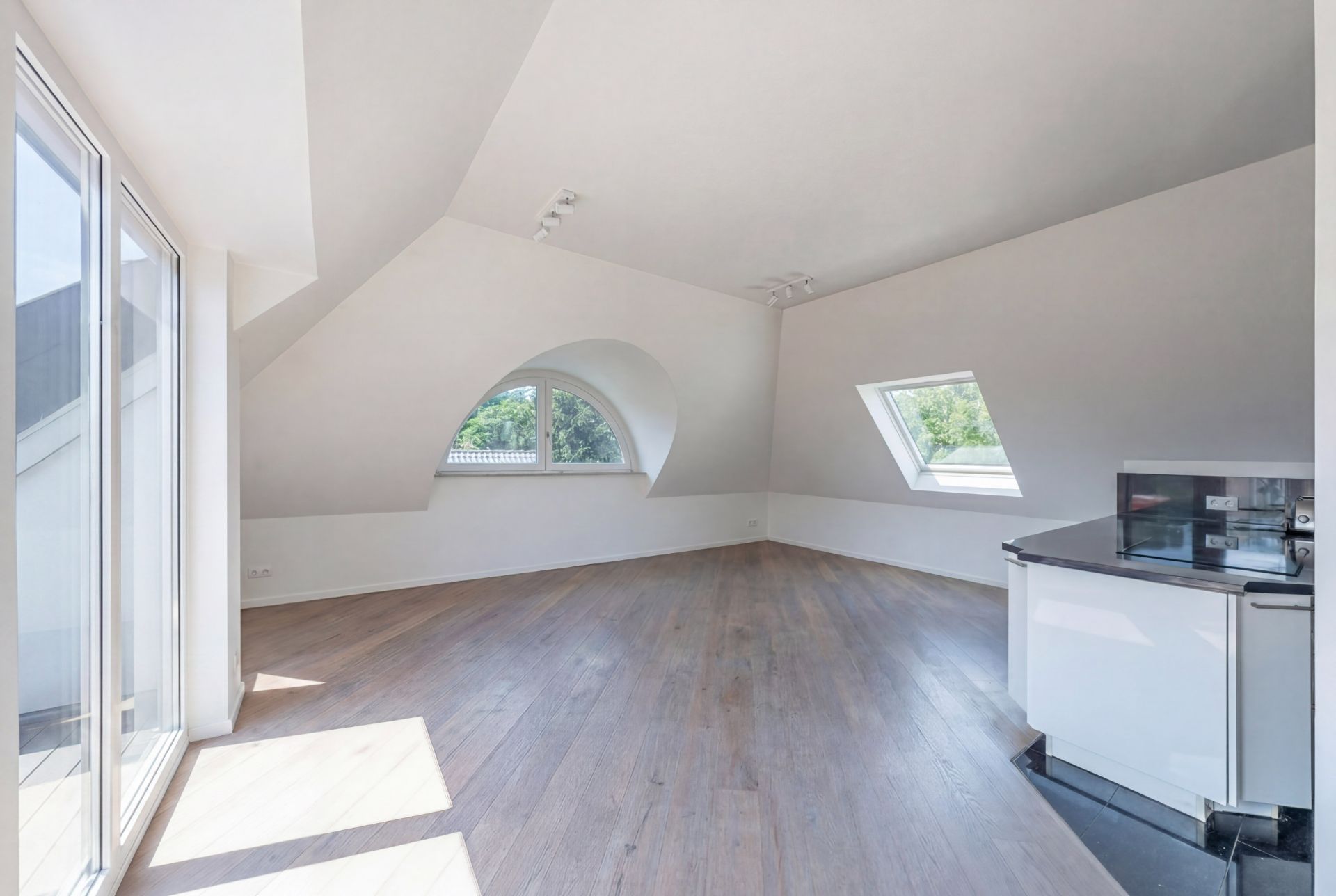 Helles Dachzimmer mit Holzboden, großen Fenstern und kleiner Küchenzeile.