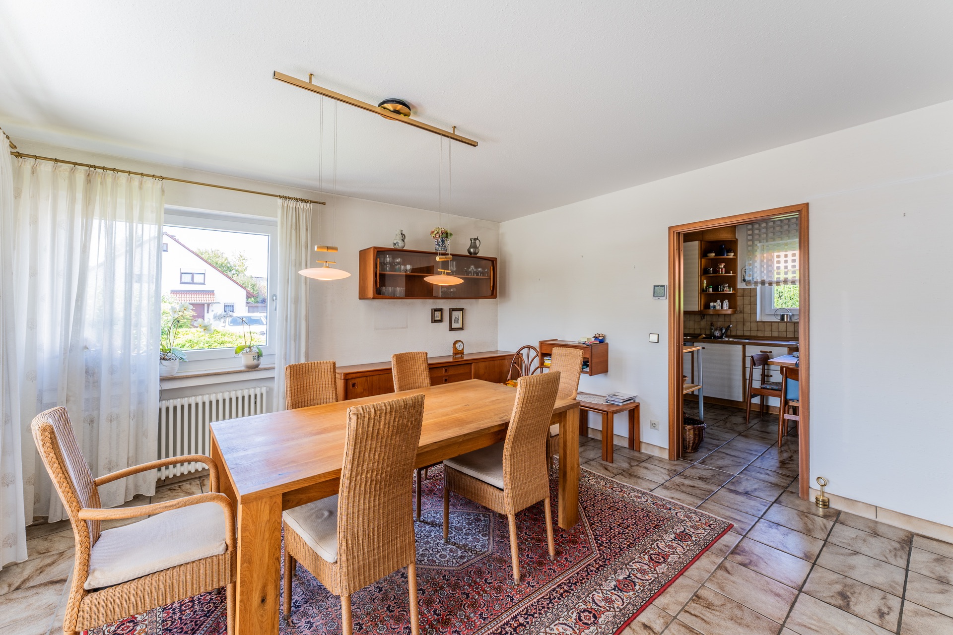 Esszimmer mit Holztisch, Stühlen, Teppich und Blick in eine angrenzende Küche.