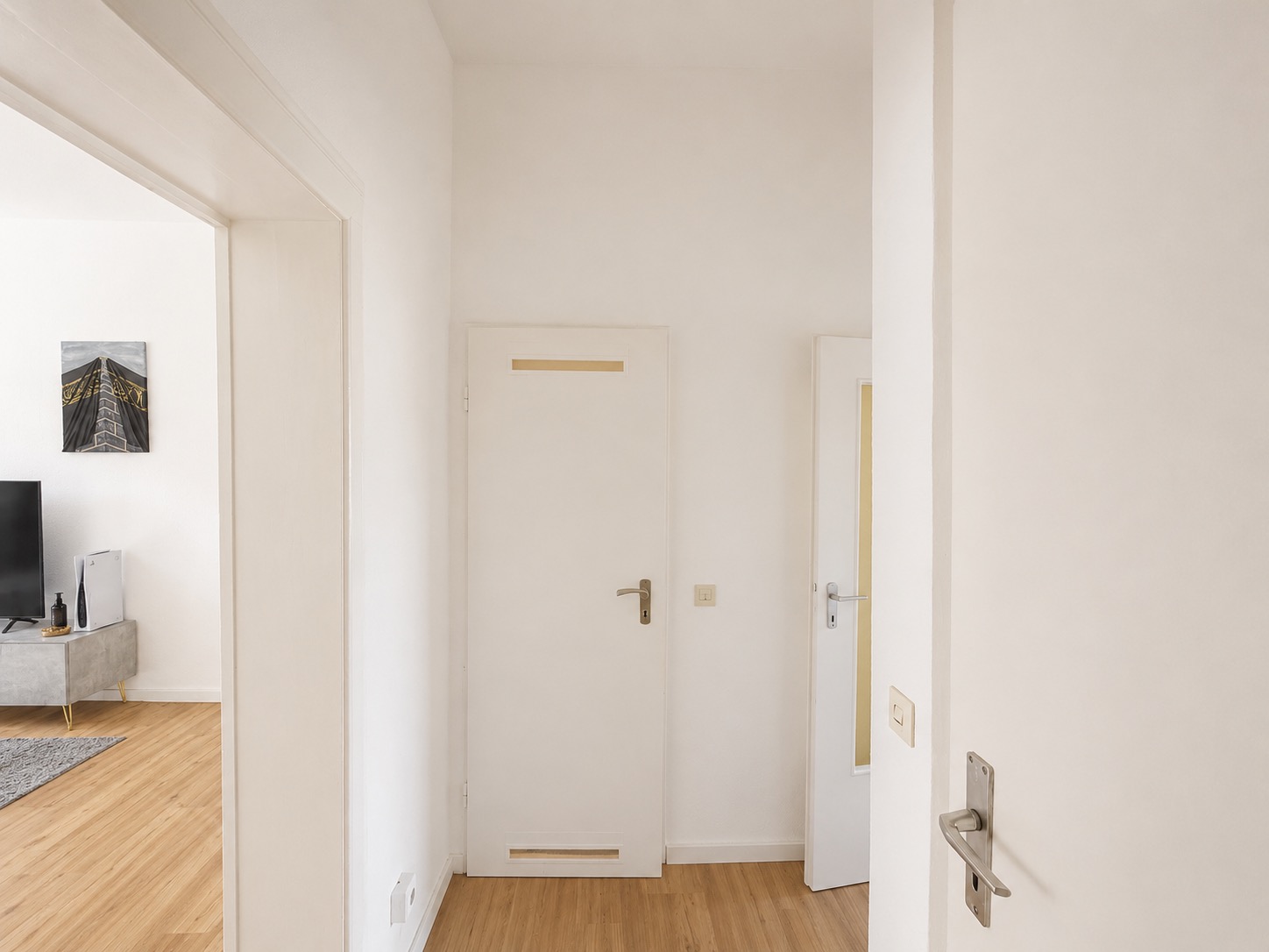 Heller Flur mit Holzboden, Türen und Blick in ein Wohnzimmer mit Fernseher.