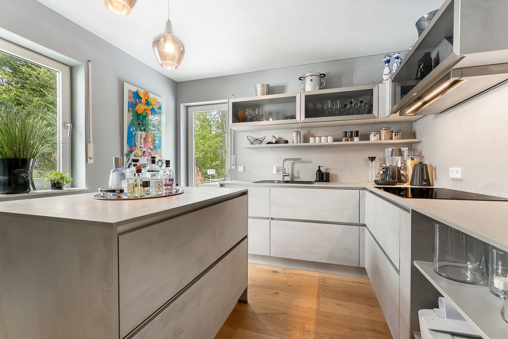 Moderne Küche mit grauen Schränken, großer Arbeitsinsel und Holzboden, Fenster und Pflanzen.