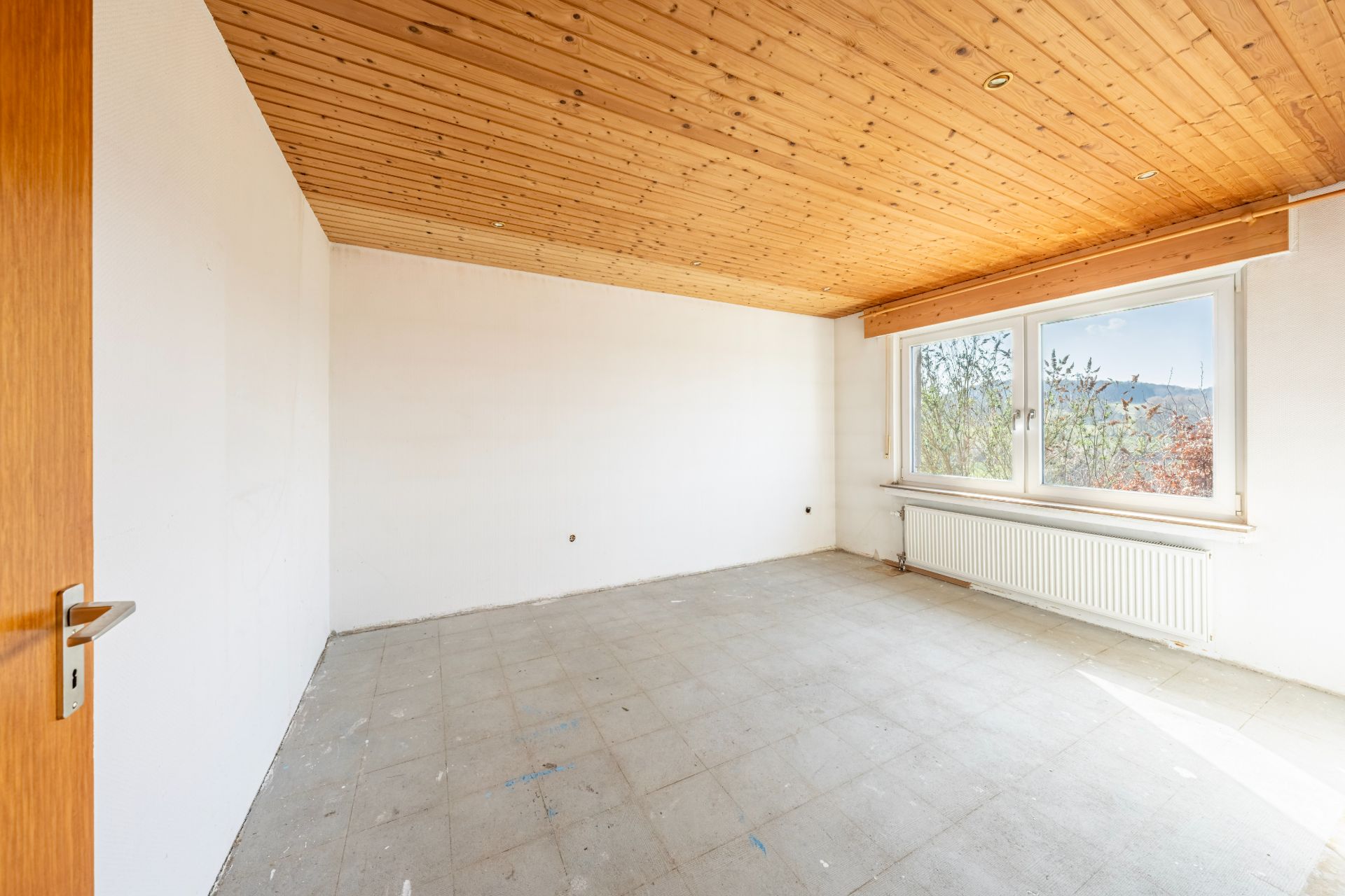 Leerer Raum mit Holzdecke, großem Fenster und Heizung unter dem Fenster.