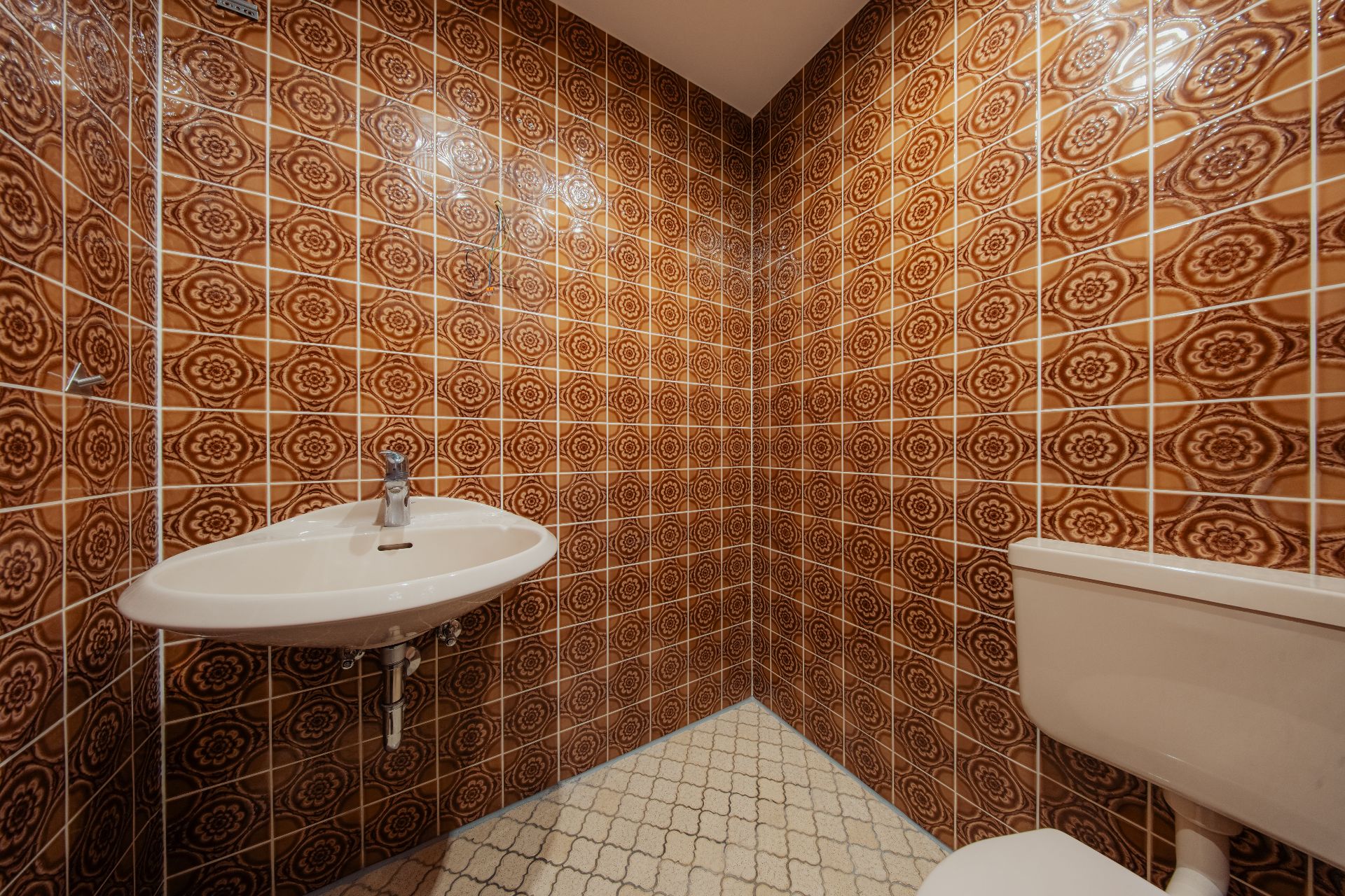 Kleines Bad mit gemusterten braunen Fliesen, Waschbecken und Toilette.