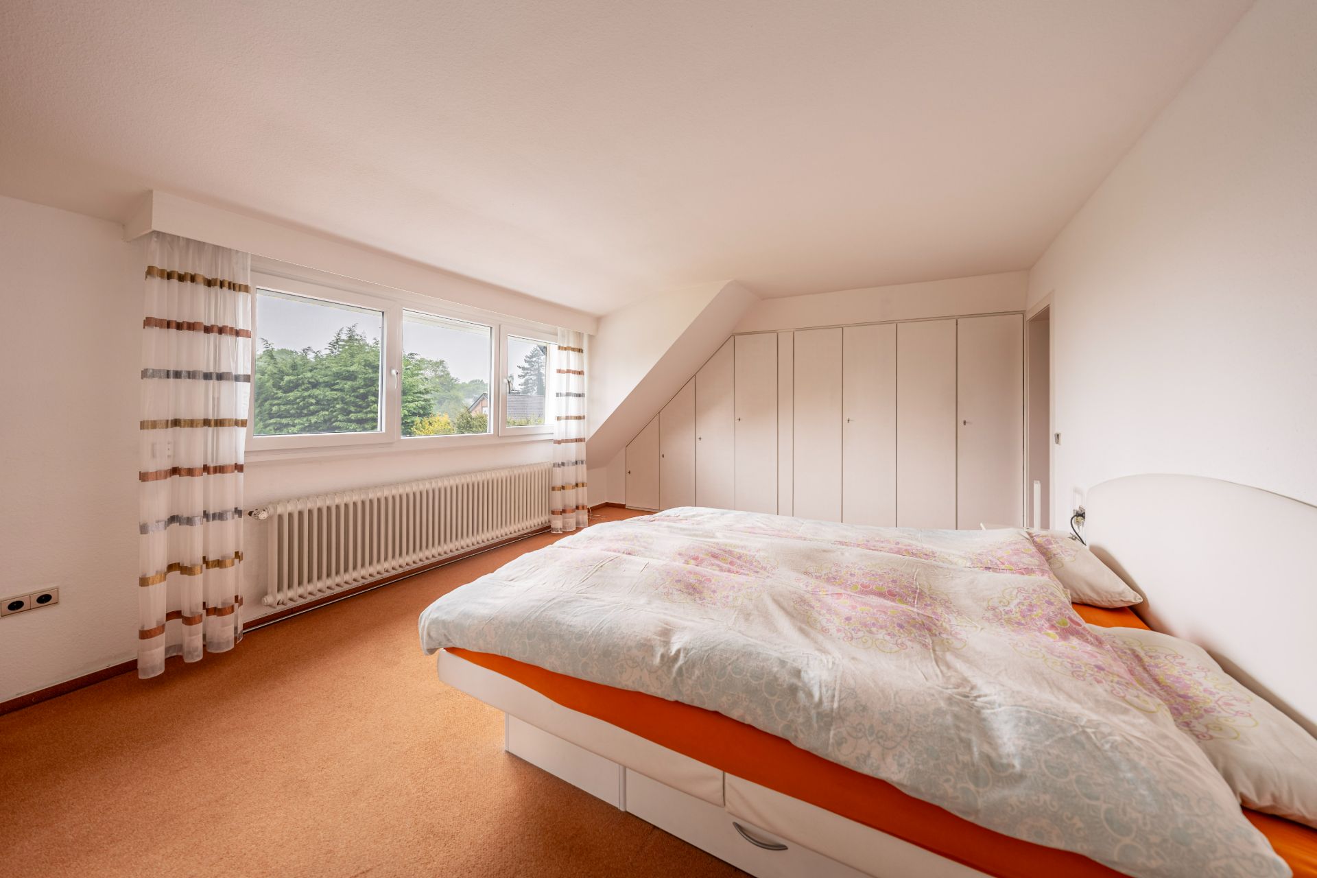 Helles Schlafzimmer mit großem Bett, Einbauschränken und Fenstern mit Blick ins Grüne.