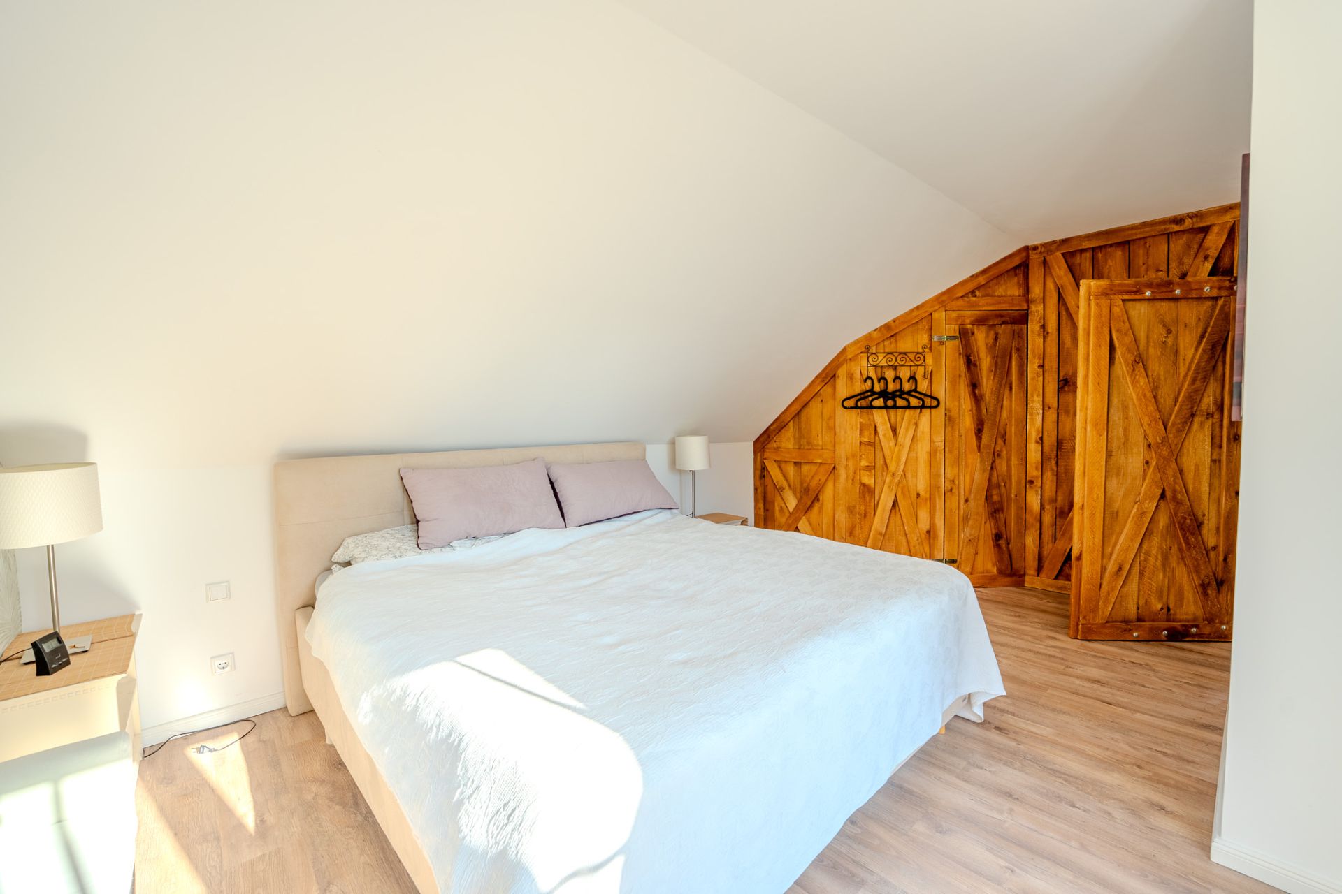 Helles Schlafzimmer mit Doppelbett, Nachttischen und Schrank mit Holztüren unter einer Dachschräge.