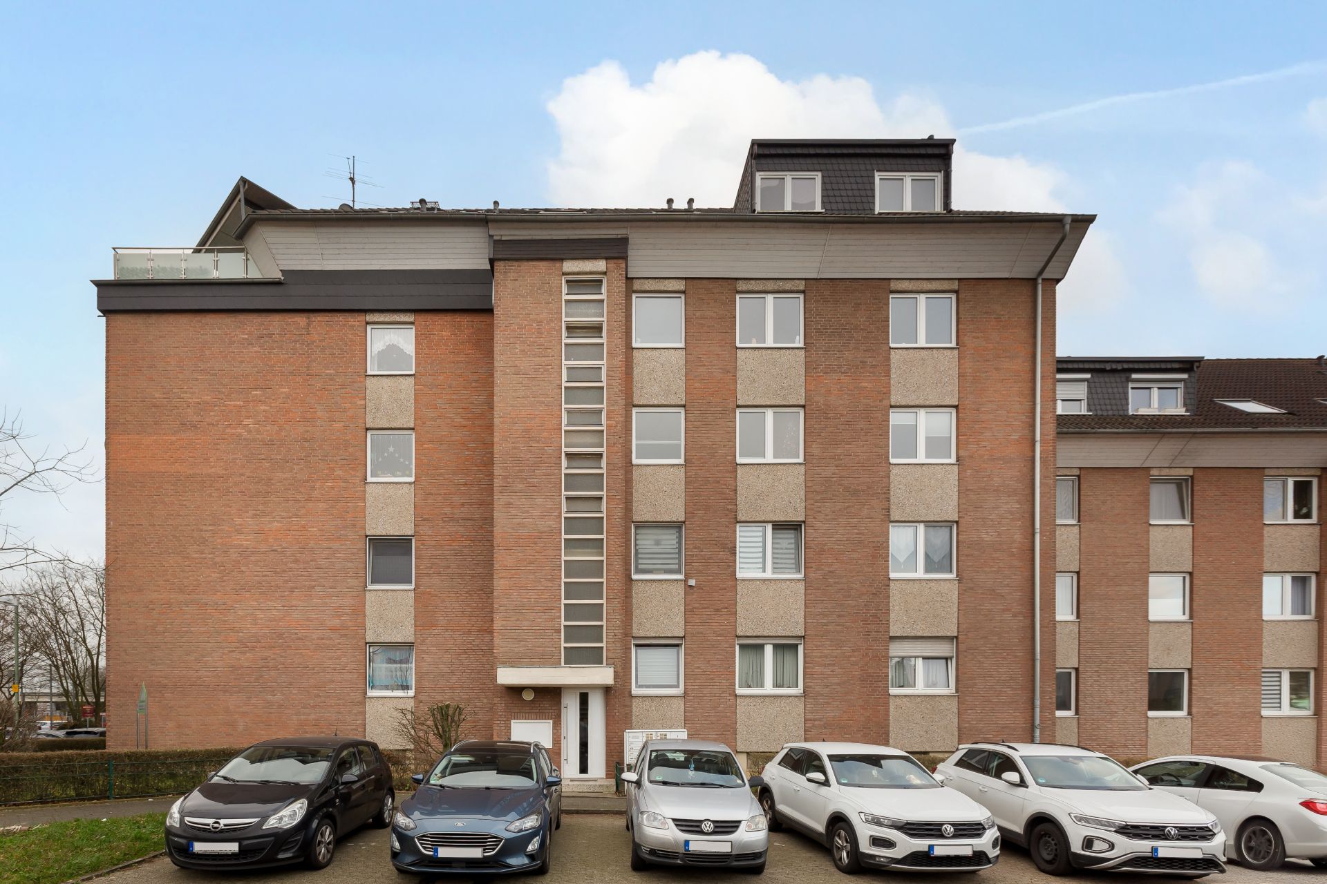 Mehrfamilienhaus aus rotem Backstein mit mehreren geparkten Autos davor.