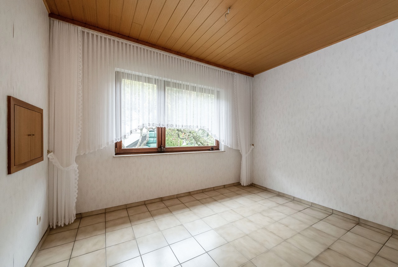 Leerer Raum mit Fliesenboden, Holzdecke und großem Fenster mit weißen Gardinen.