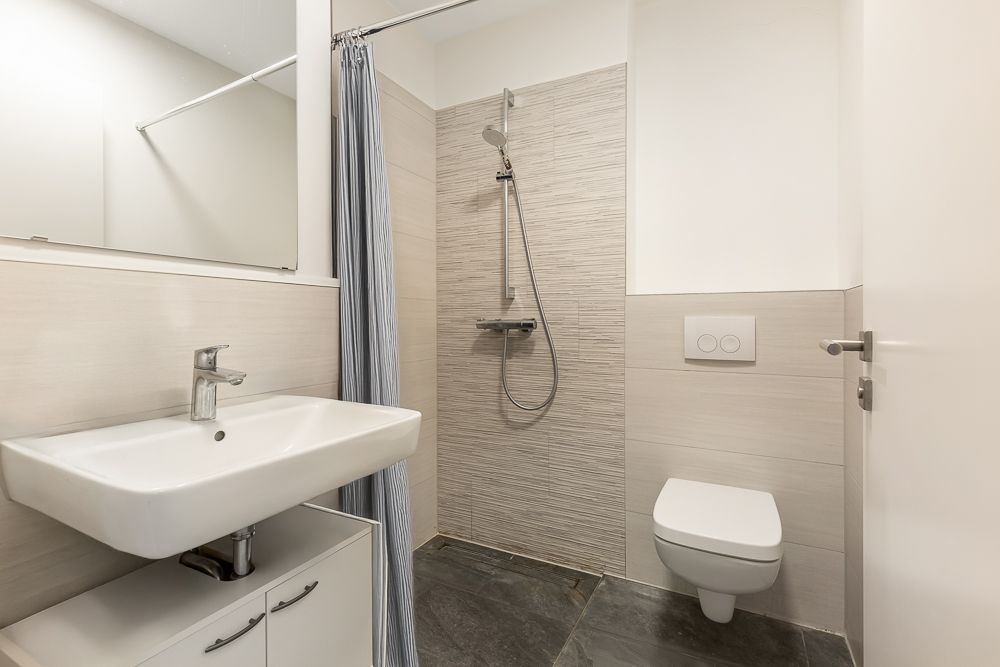 Modernes Badezimmer mit Waschbecken, Dusche mit Vorhang und Wandtoilette.