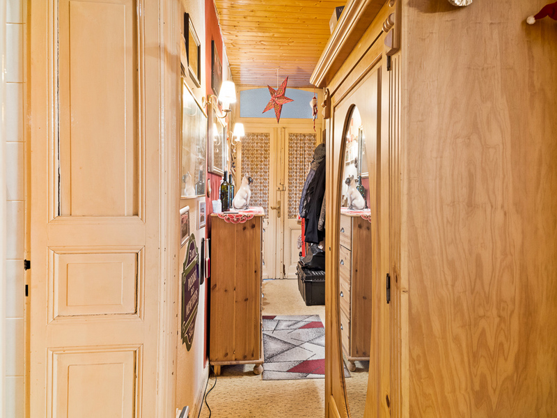 Schmaler Flur mit Holzschrank, Spiegel, Kommode und leuchtender Wandlampe.
