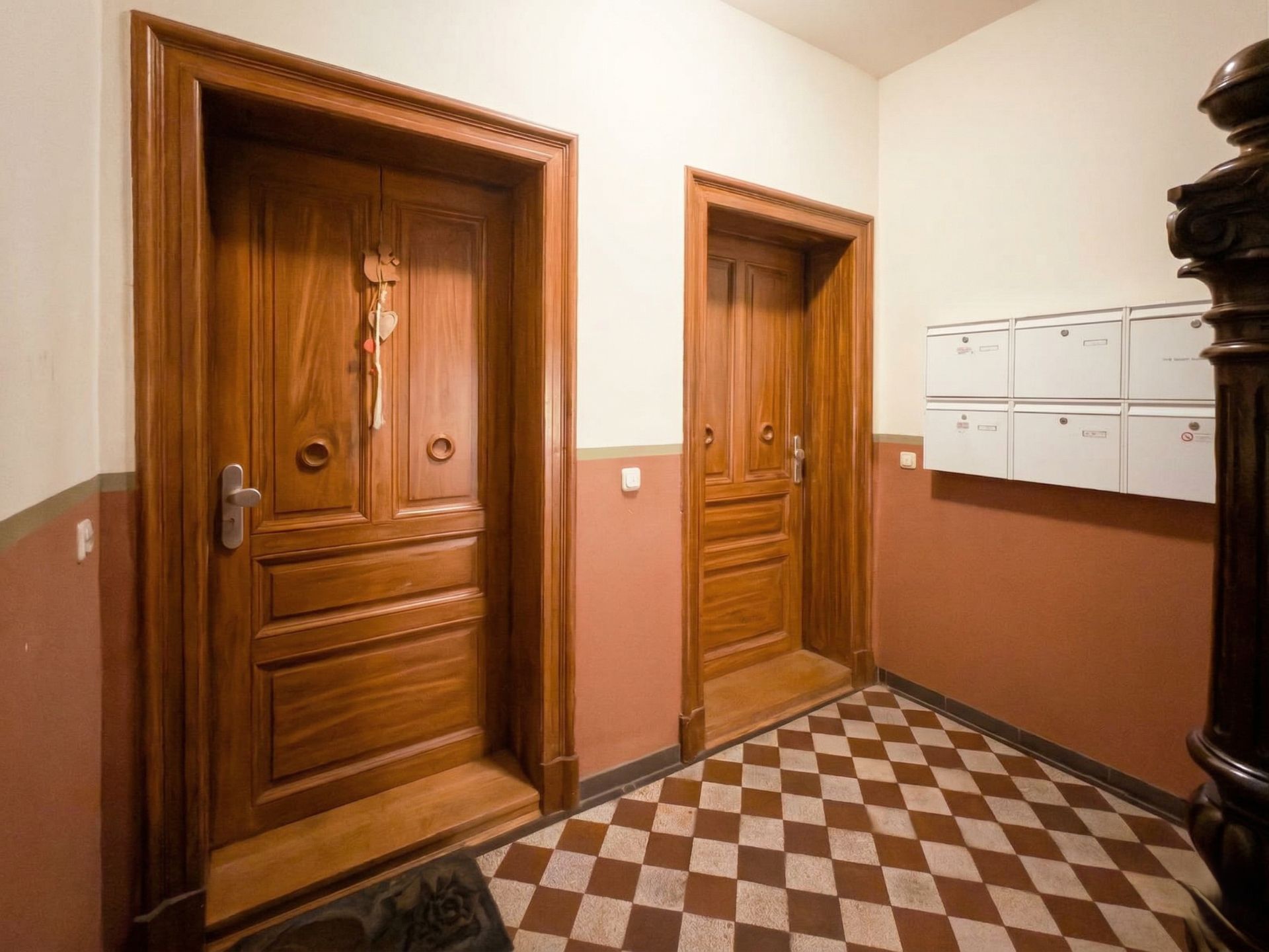 Hausflur mit zwei Holztüren, Briefkästen und kariertem Boden.