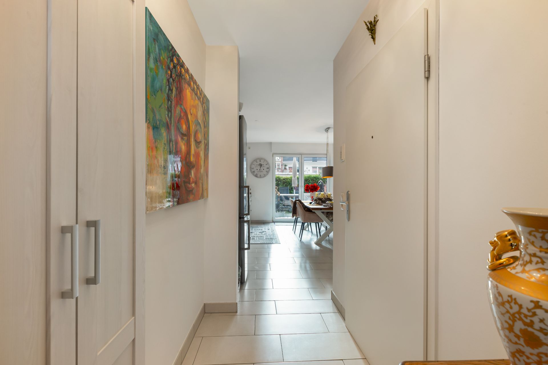 Flur mit Schrank, bunter Wandkunst, Keramikvase und Blick ins Esszimmer mit Fenster.