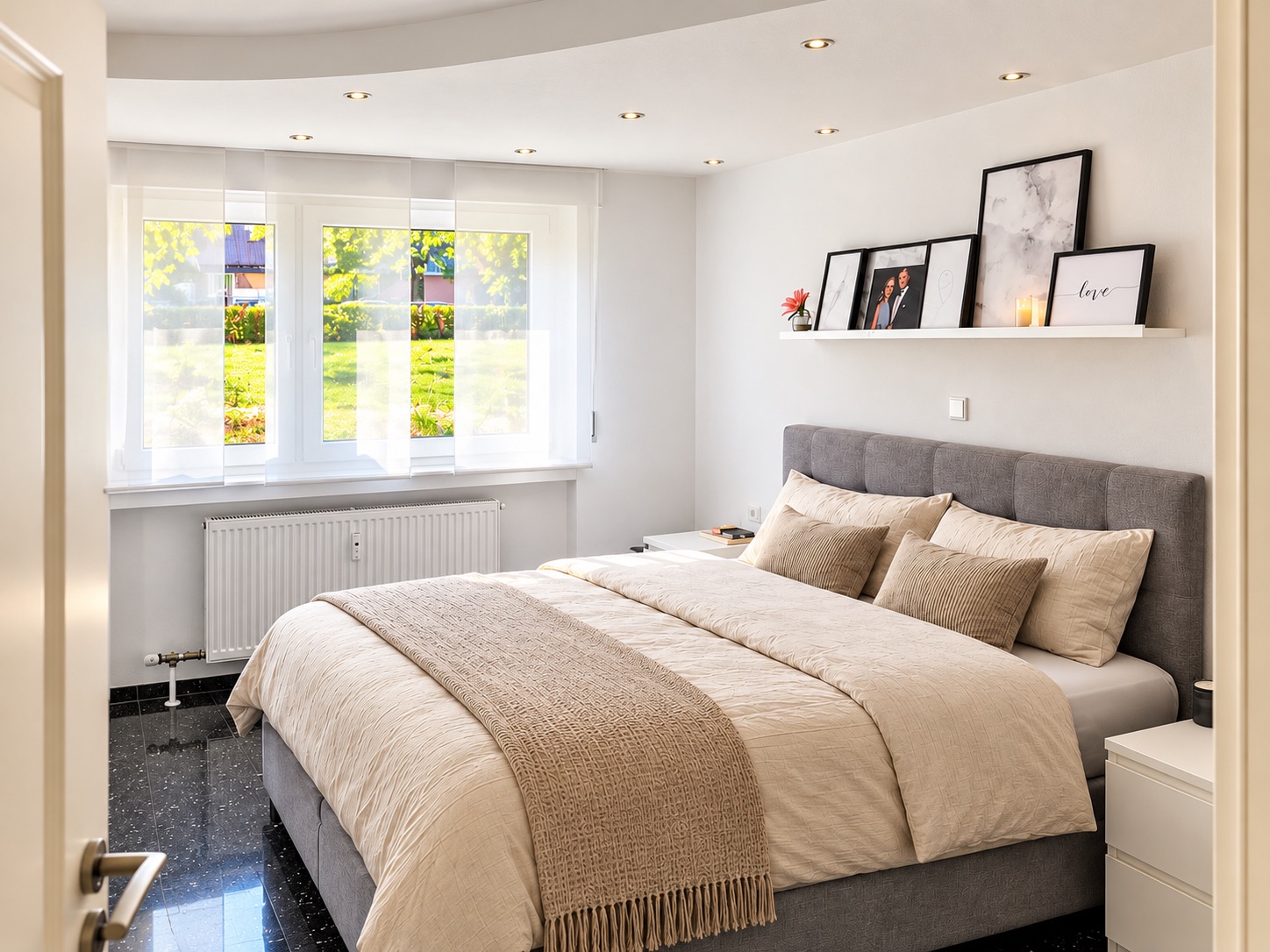 Helles Schlafzimmer mit großem Bett, drei Fenstern und einer Wandablage mit Bildern.