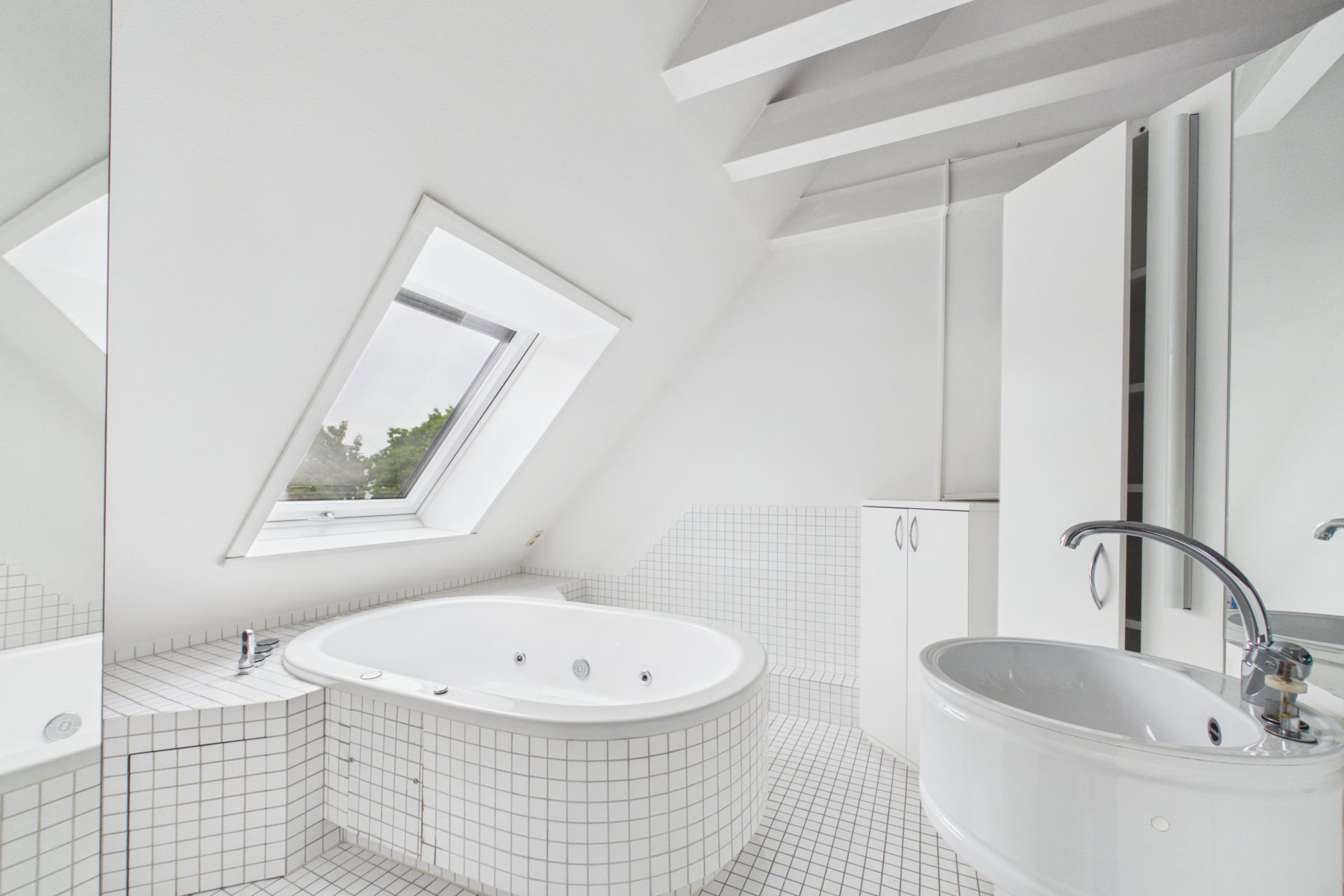 Helles Badezimmer mit runder Badewanne, Waschbecken und Dachfenster.