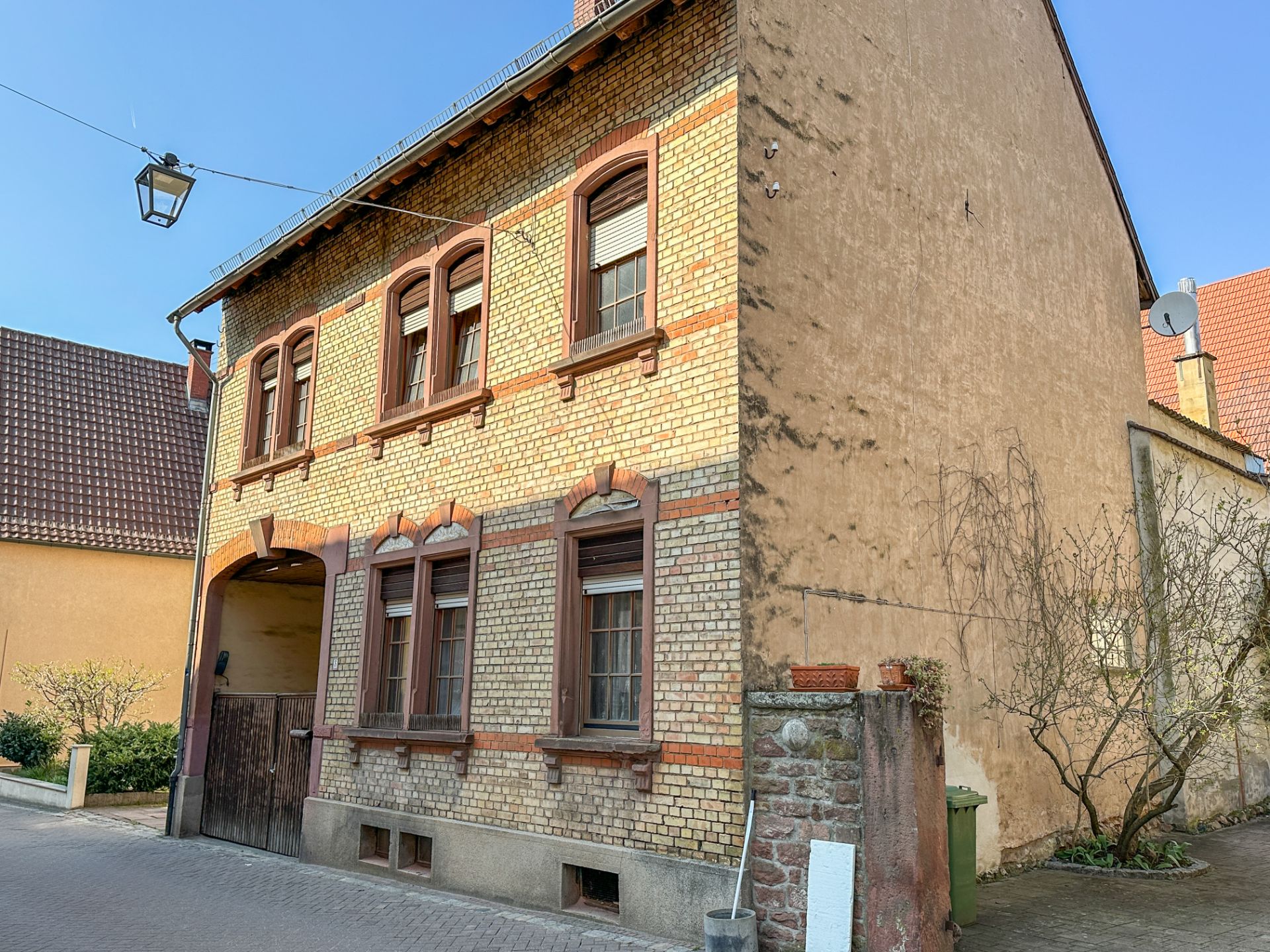 Zweistöckiges Haus mit gelber Backsteinfassade und Holztoren an einer ruhigen Straße.