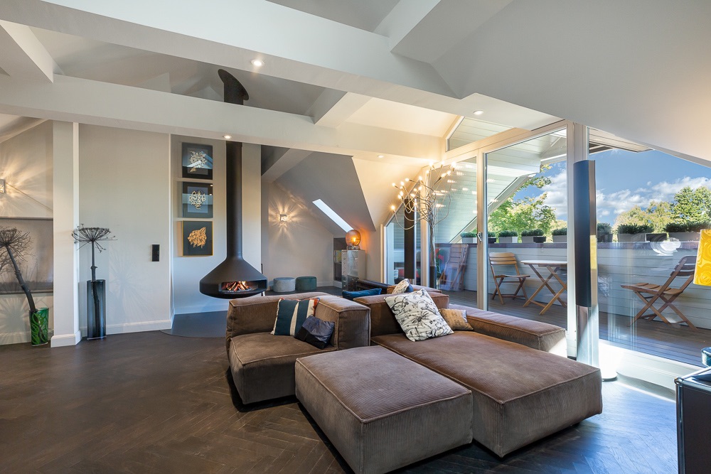 Modernes Wohnzimmer mit Ecksofa, Hängerkamin und Zugang zu einer Terrasse mit Sitzmöbeln.