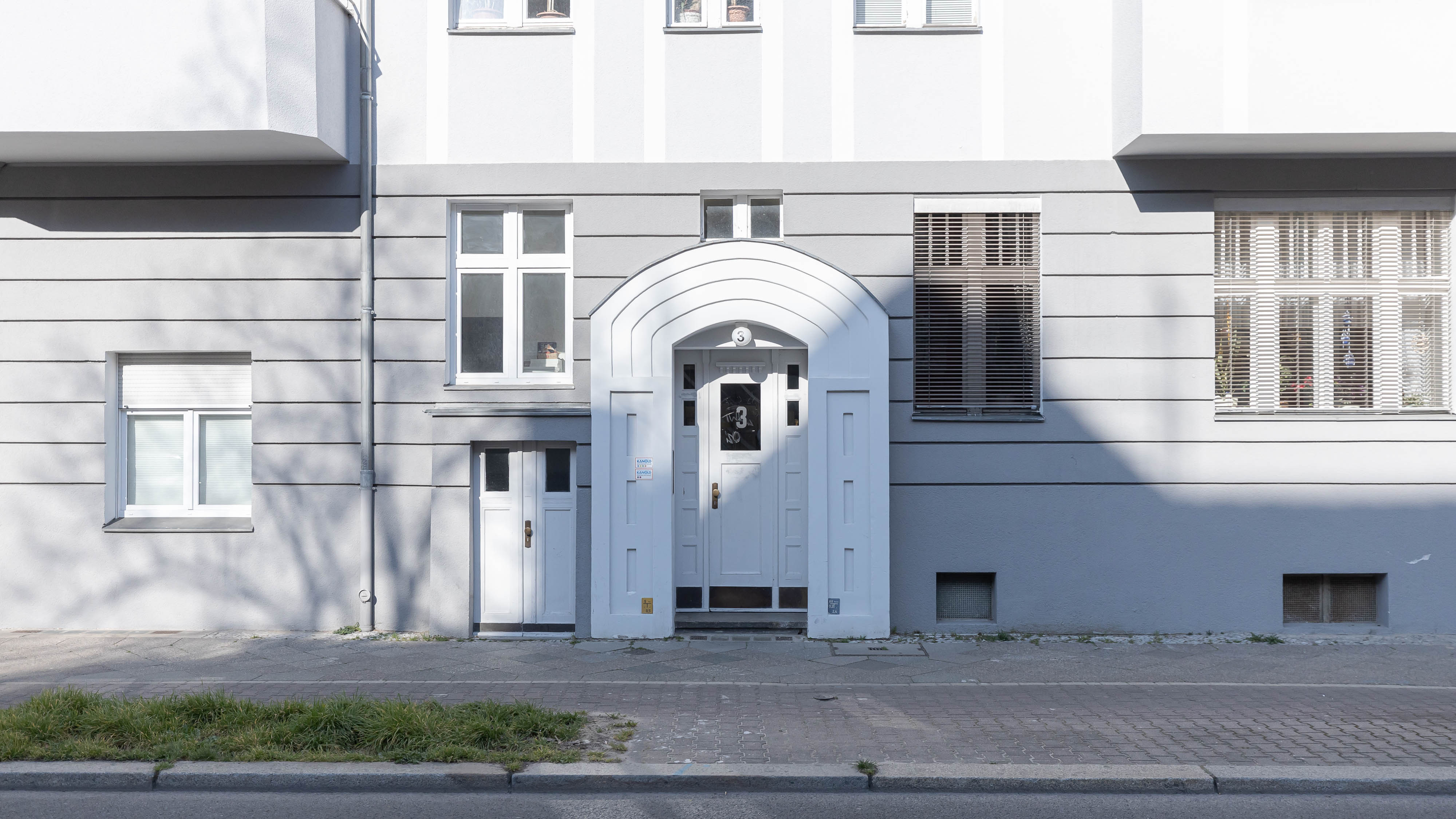 Eingangstür eines Wohngebäudes mit mehreren Fenstern und grauer Fassade.