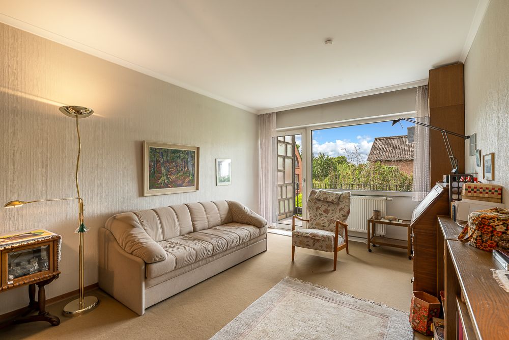 Helles Wohnzimmer mit Sofa, Sessel, Teppich und offenem Zugang zum Garten.