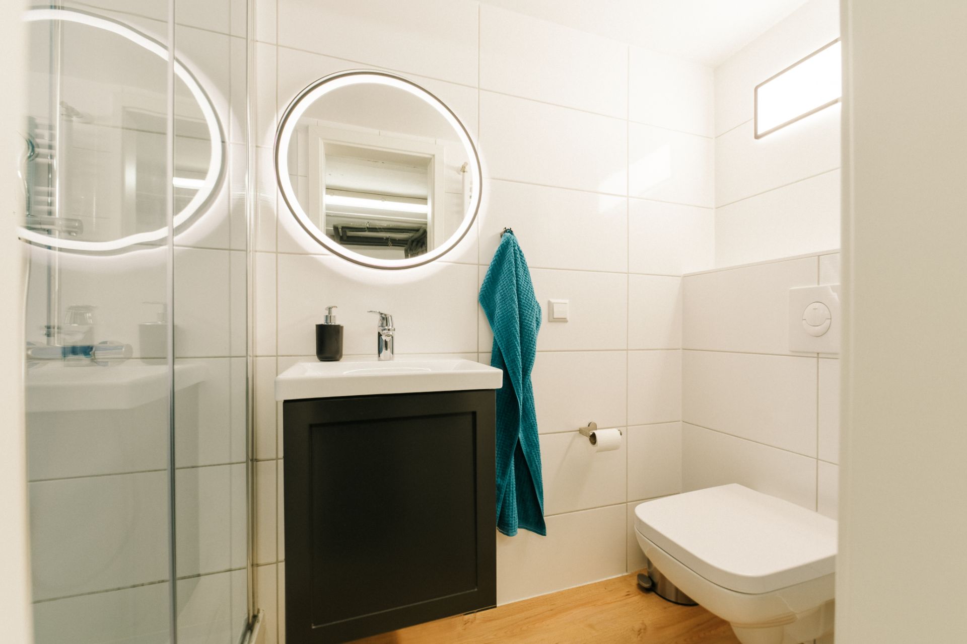 Modernes Badezimmer mit Waschbecken, rundem Spiegel, Handtuch und Toilette.