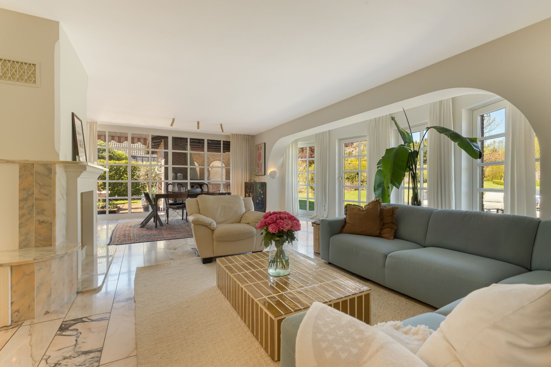 Helles Wohnzimmer mit Sofas, Couchtisch, Pflanze und großen Fenstern mit Blick nach draußen.