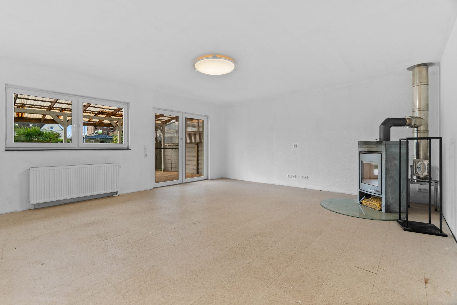 Helles Wohnzimmer mit Kaminofen, großen Fenstern und Zugang zur Terrasse.