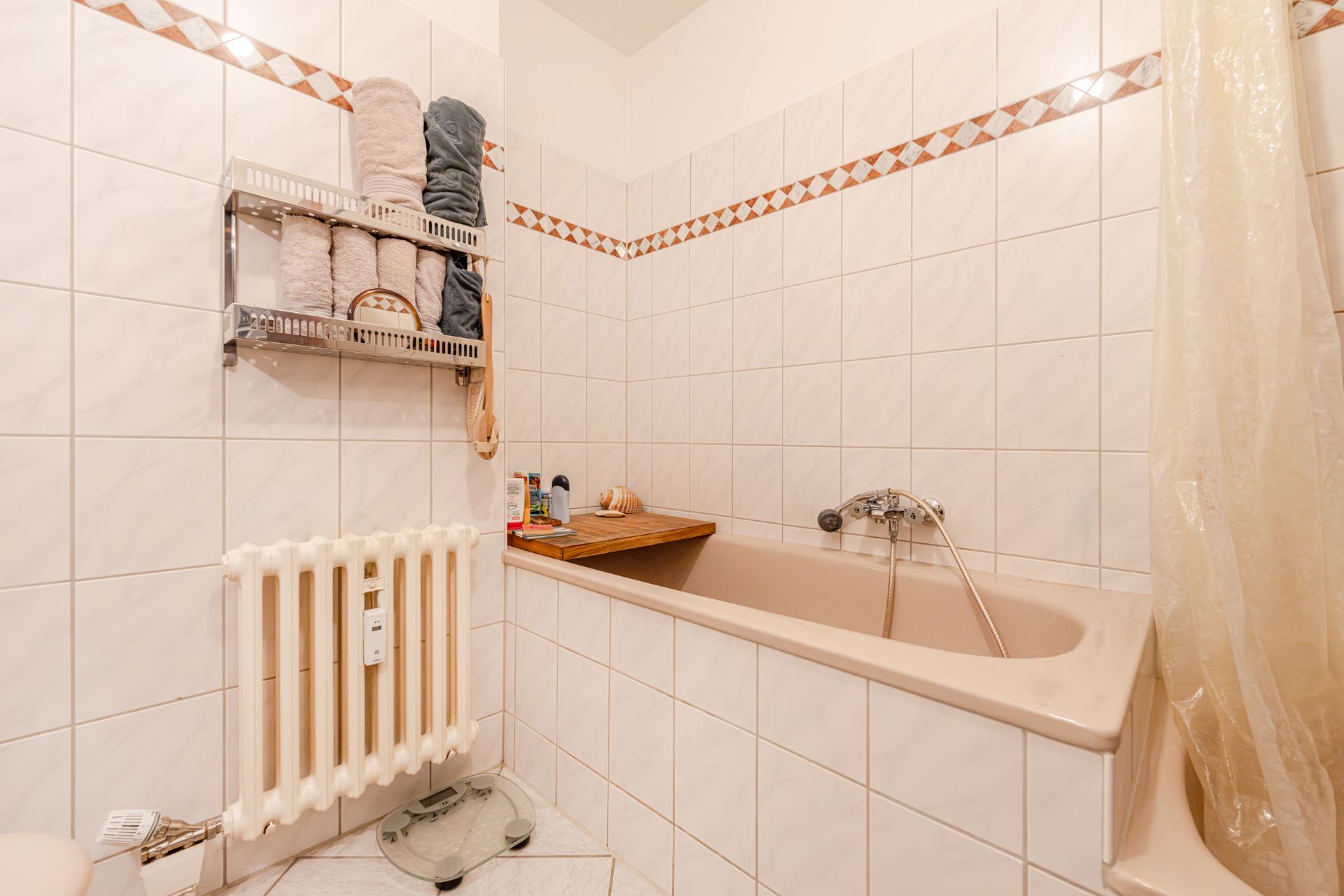 Badezimmer mit Badewanne, Handtuchregal, Heizkörper und Fliesenwänden.