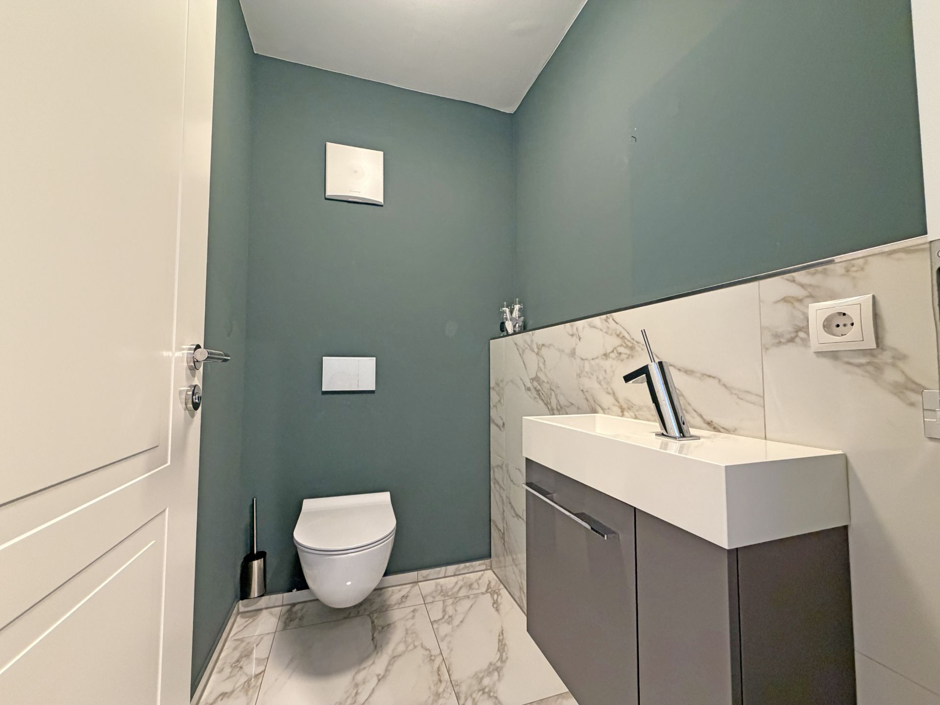 Modernes Badezimmer mit hängender Toilette und Waschbecken, Wand in Grün, Boden in Marmoroptik.