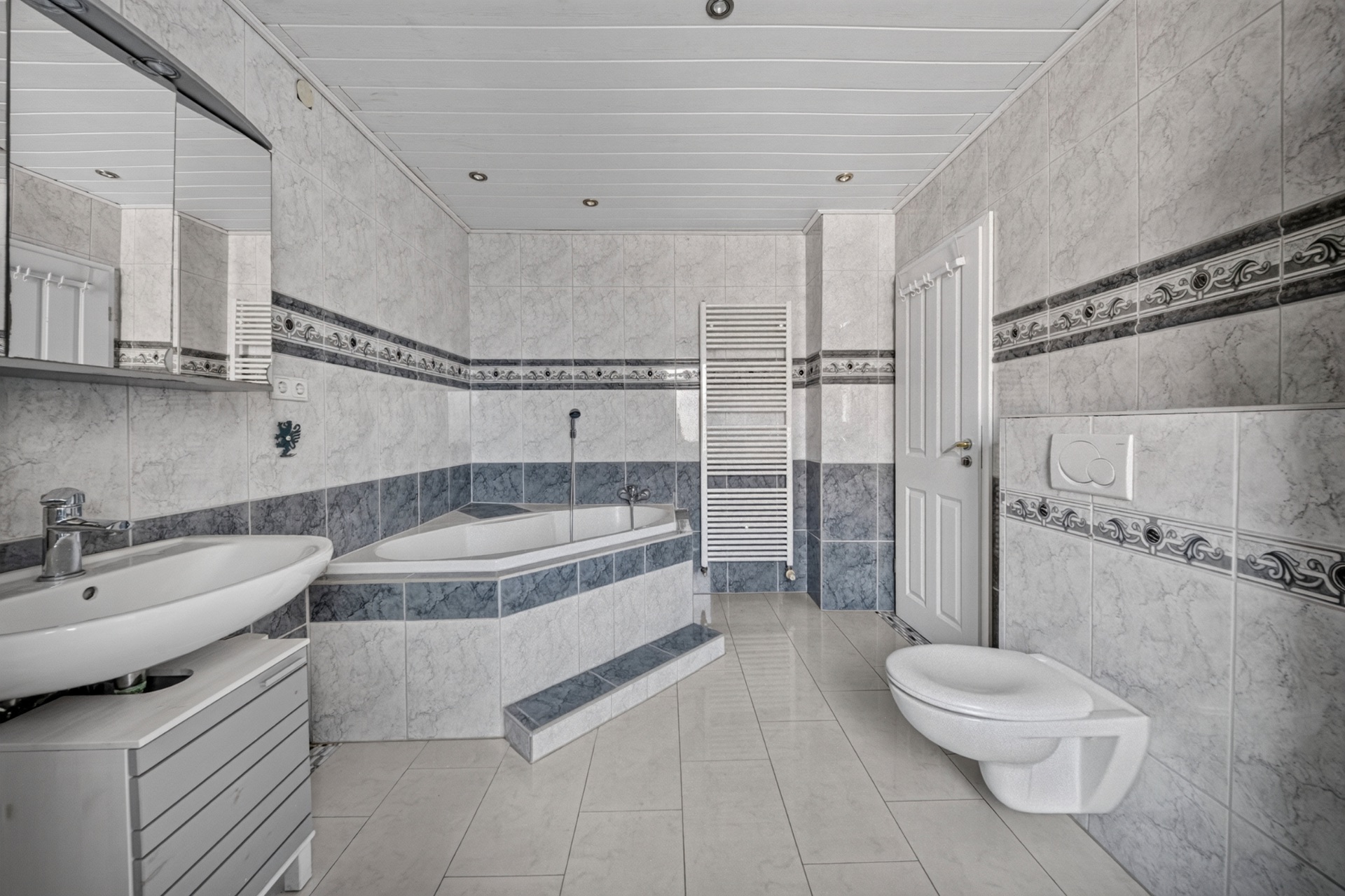 Modernes Badezimmer mit Eckbadewanne, Waschbecken, Wandtoilette und Handtuchheizkörper.