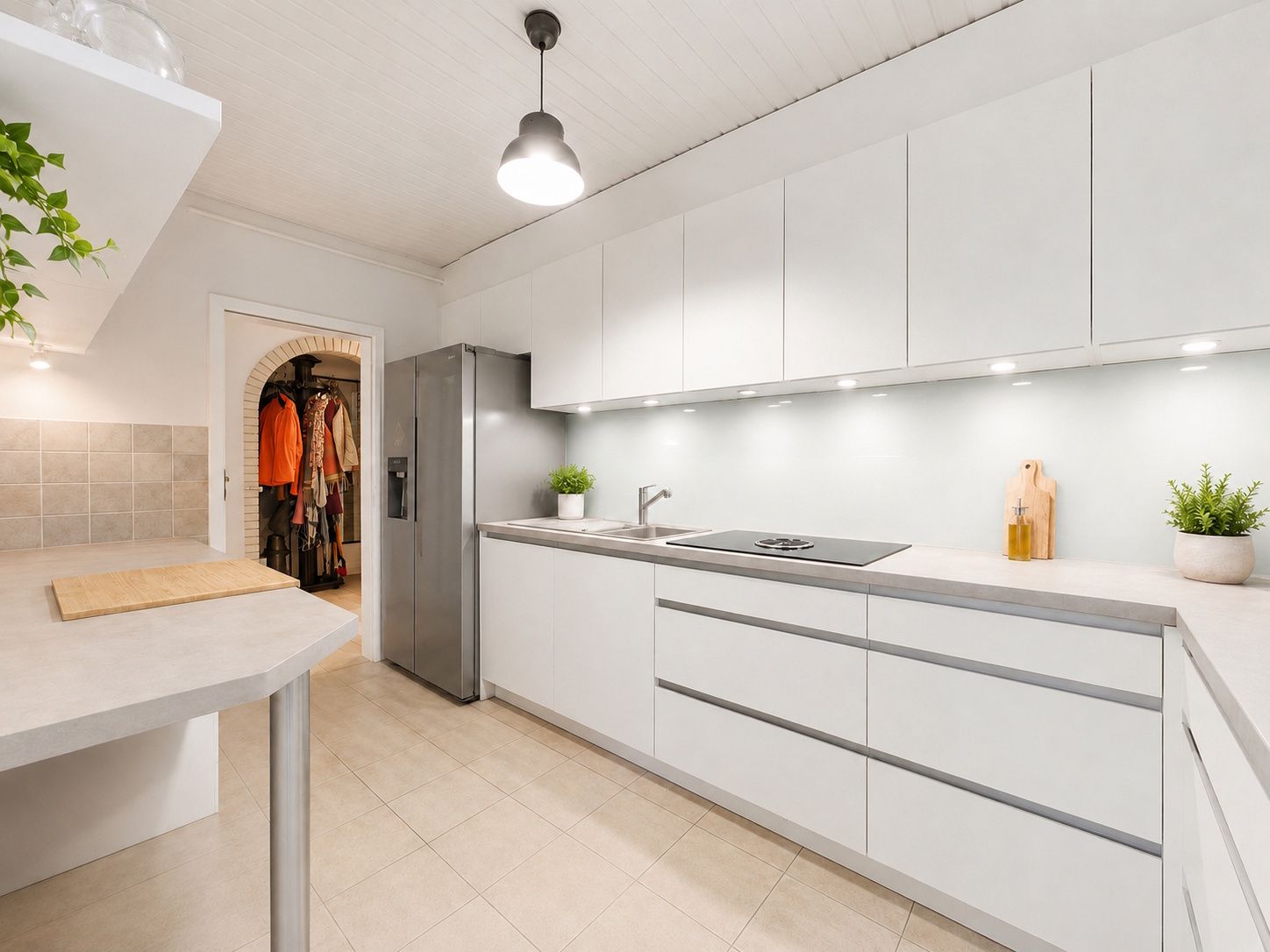 Moderne, helle Küche mit weißen Schränken, großem Kühlschrank und Pflanzen auf der Arbeitsfläche.