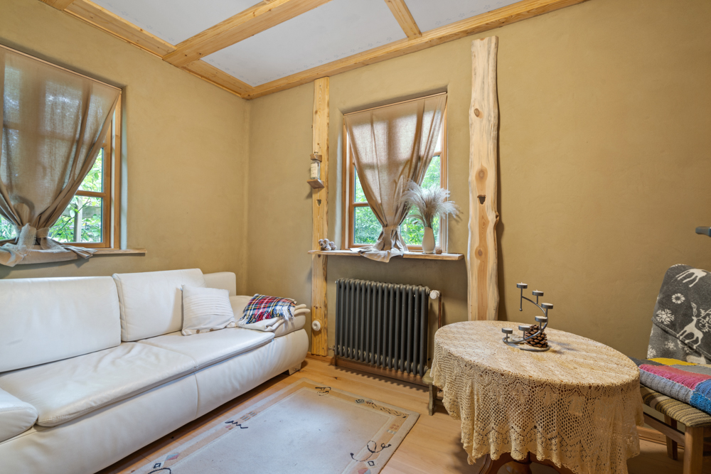 Gemütliches Wohnzimmer mit weißem Sofa, Holztisch, Teppich und zwei Fenstern mit Gardinen.
