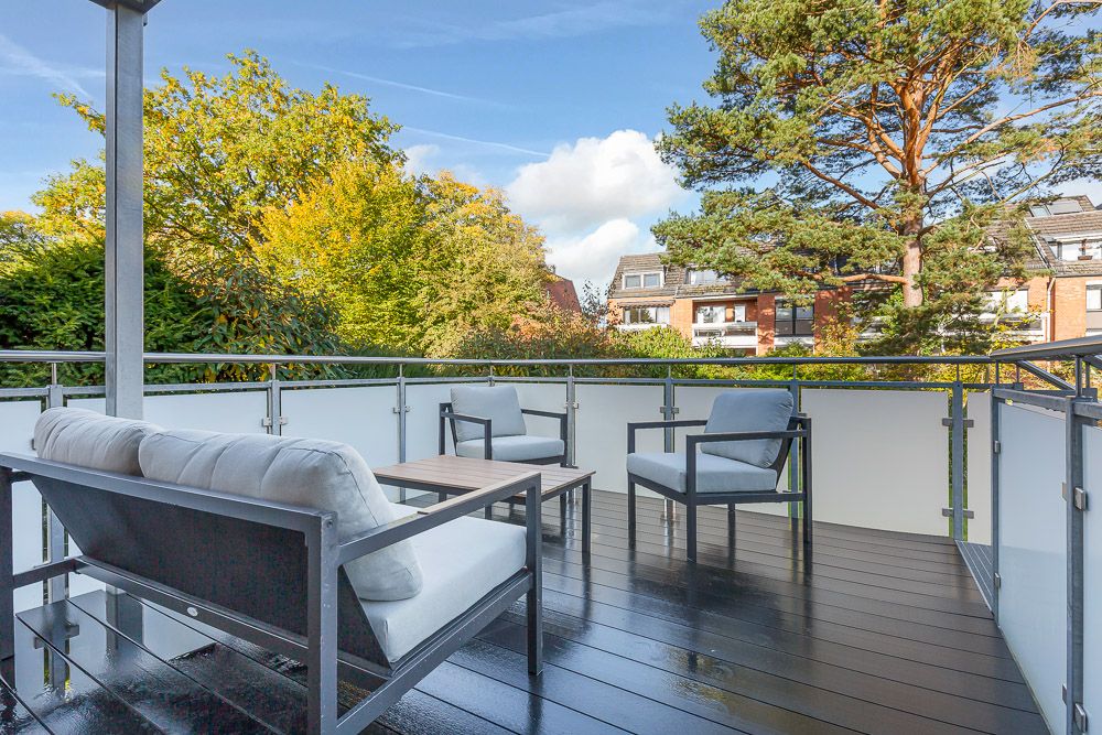 Moderne Terrasse mit Sitzmöbeln, Tisch und Blick auf Bäume sowie Nachbarhäuser.