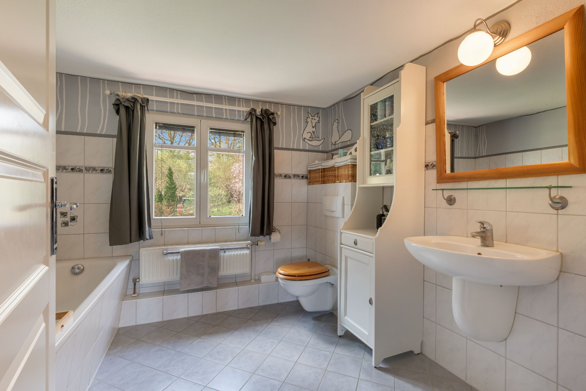 Helles Badezimmer mit Fenster, Badewanne, Waschbecken, Toilette und Hängeschrank.