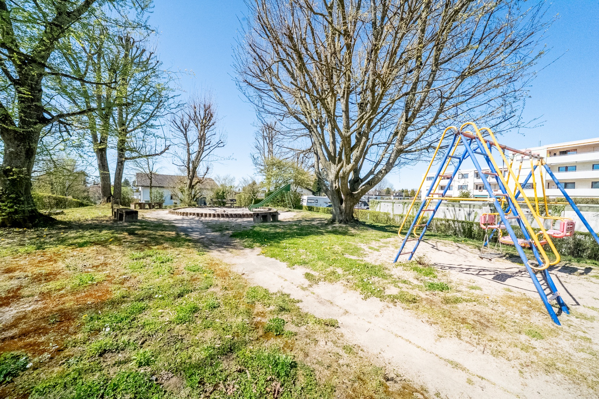 Garten mit großem Baum, Sandkasten, Sitzbänken und blauer Kinderschaukel.