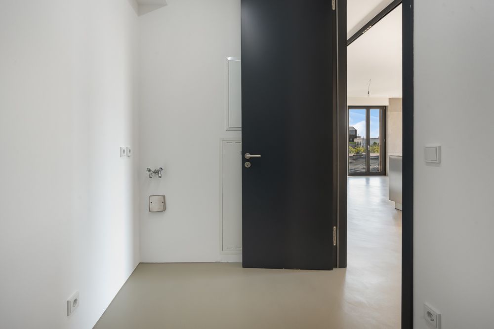 Leerer, heller Raum mit offenstehender dunkler Tür und sichtbaren Anschlüssen an der Wand.