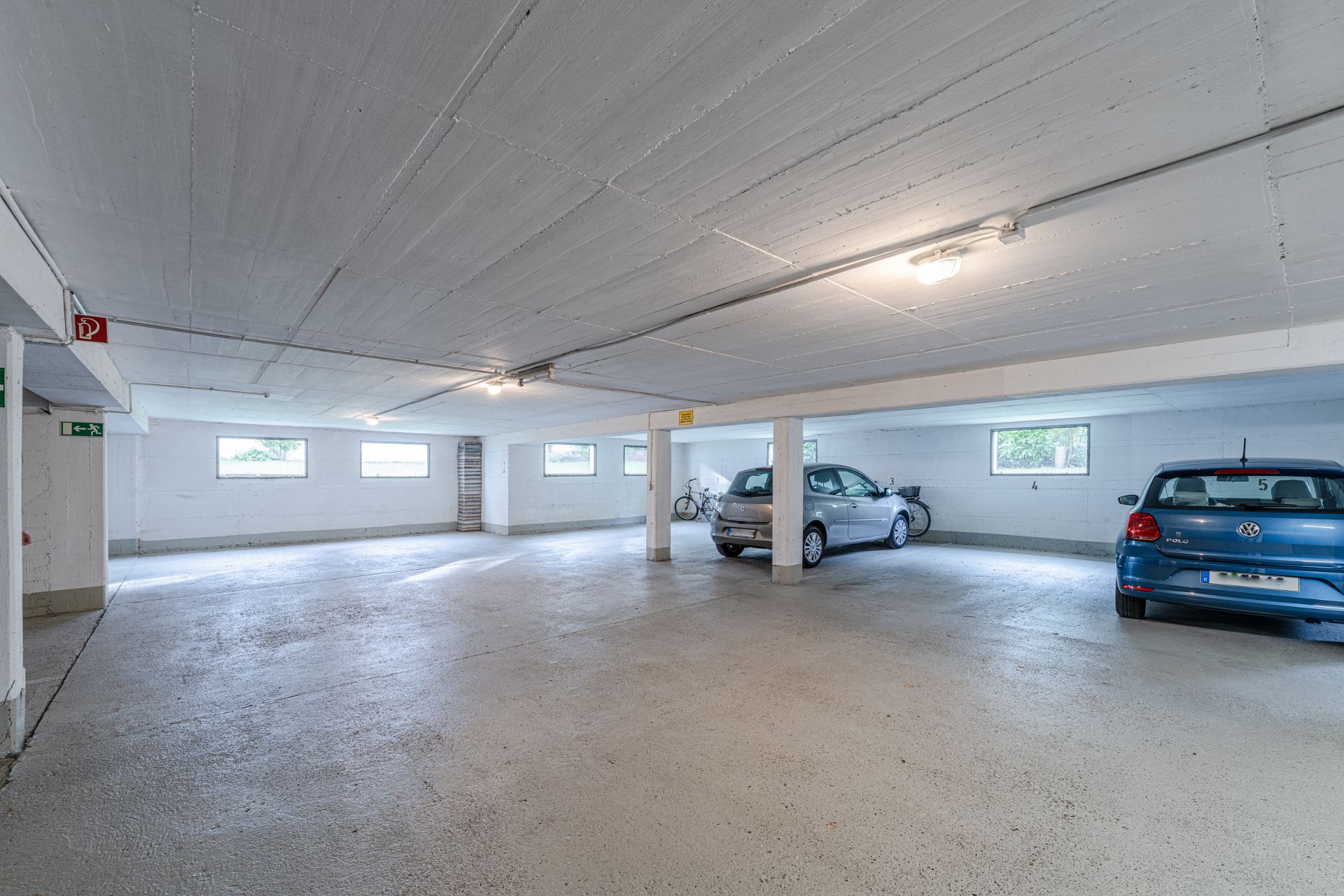 Helle Tiefgarage mit zwei geparkten Autos und einigen Fahrrädern an der Wand.