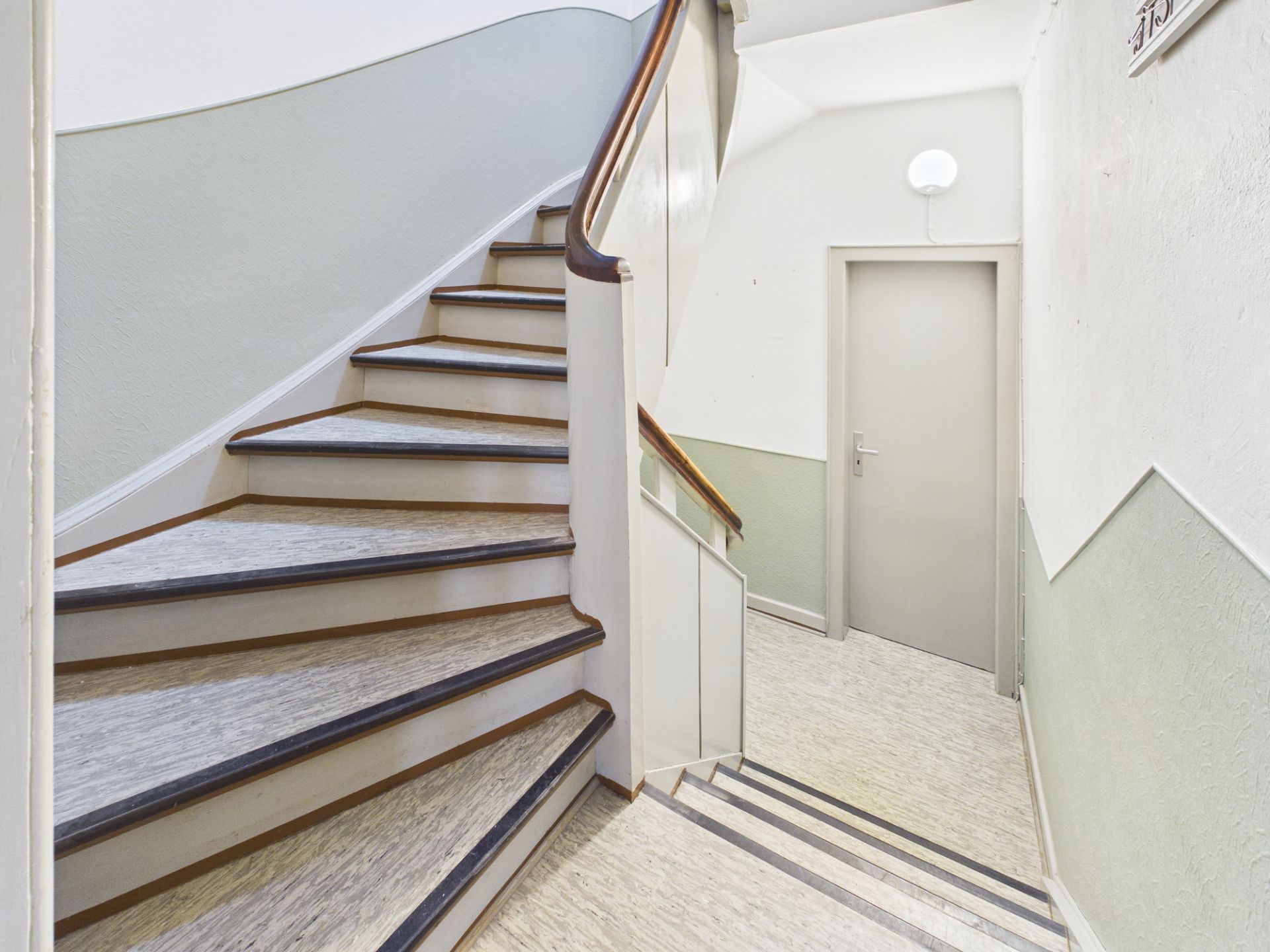 Heller Treppenhausbereich mit einer Holztreppe und einer geschlossenen Tür.