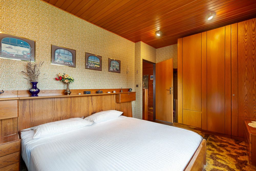 Schlafzimmer mit Holzmöbeln, Doppelbett, Blumenvasen und Bildern an der Wand.