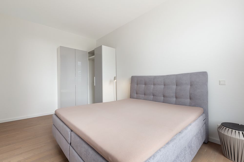Schlafzimmer mit grauem Bett, offenem Kleiderschrank und Nachttisch auf Holzboden.