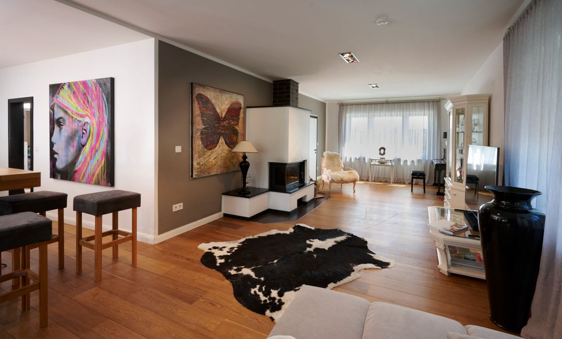 Modernes Wohnzimmer mit Holzboden, Kamin, großen Fenstern und auffälliger Wandkunst.