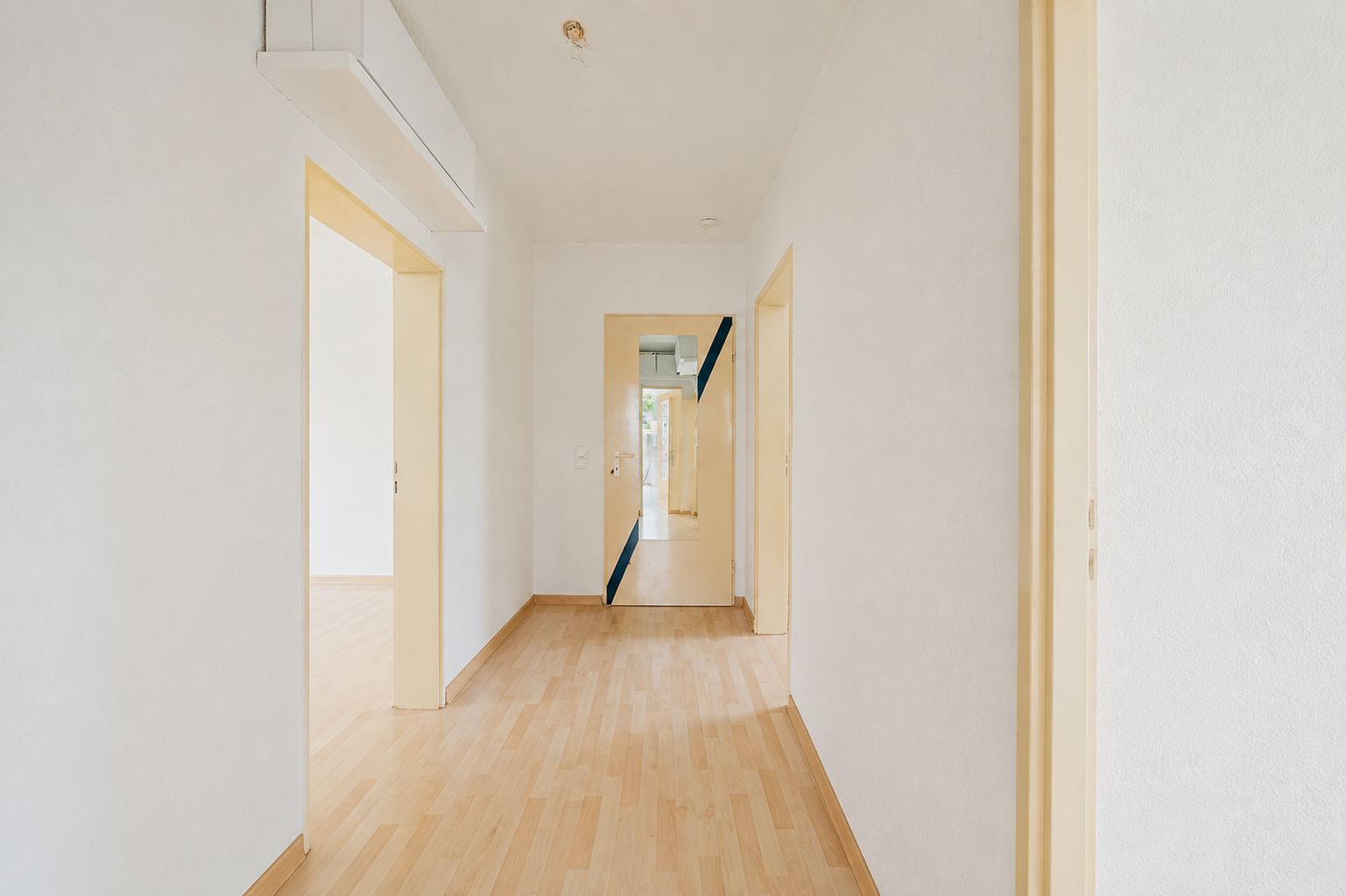 Heller Flur mit Holzboden und mehreren offenen Türen in einer Wohnung.