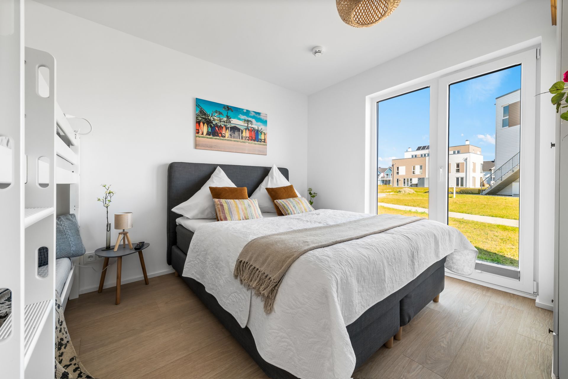 Helles Schlafzimmer mit Doppelbett, Etagenbett, großem Fenster und Blick nach draußen.