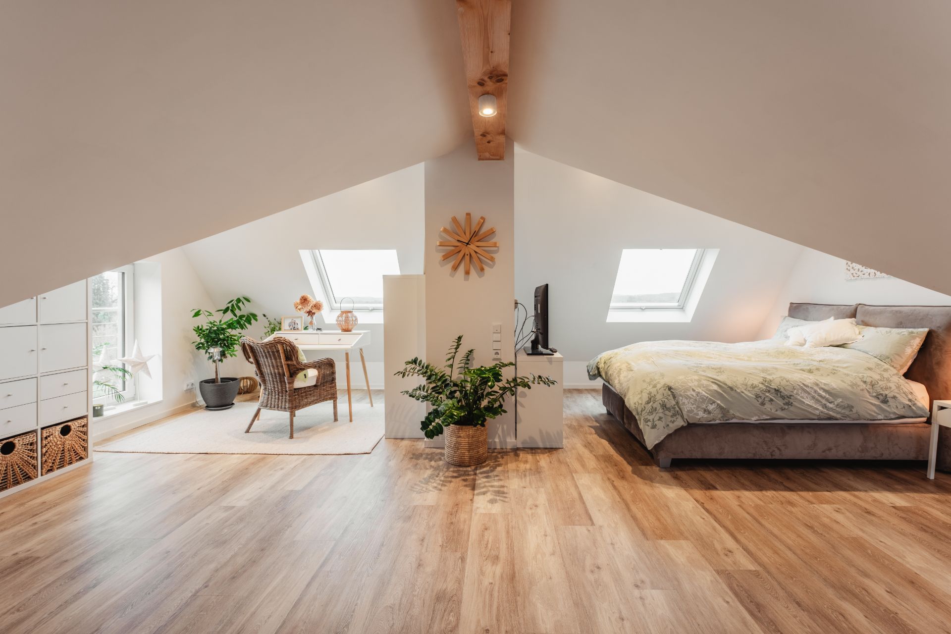 Helles Dachgeschosszimmer mit Schreibtisch, Bett, Pflanzen und Holzfußboden.