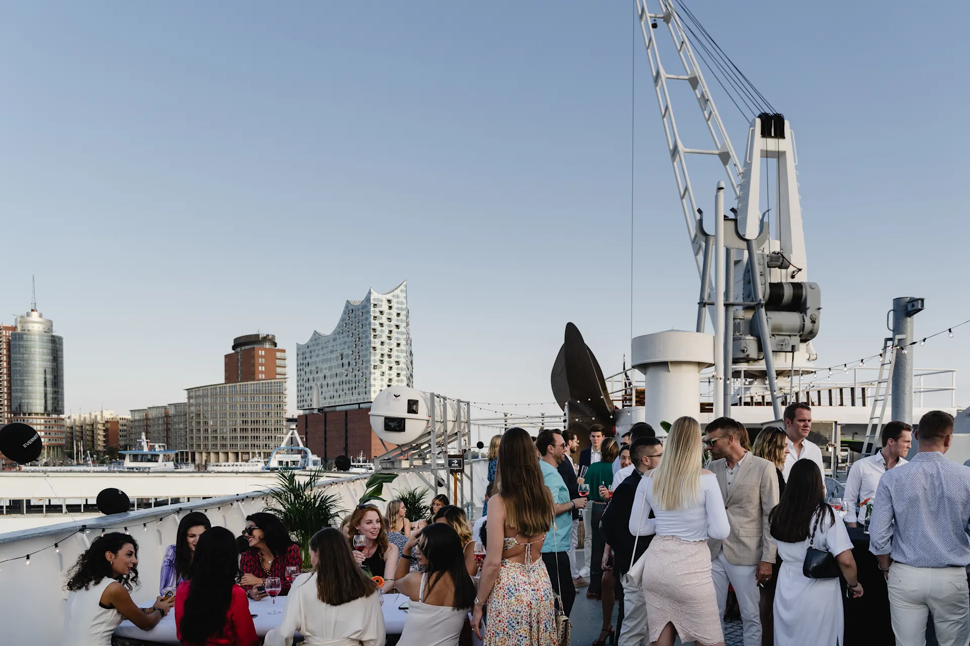 Gruppe von Menschen feiert auf einer Dachterrasse mit Blick auf die Stadt und moderne Gebäude.